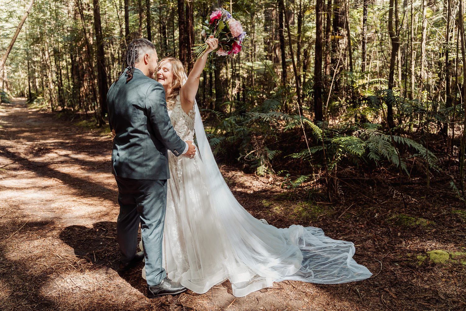 A beautiful wedding ceremony takes place on a forest trail surrounded by tall trees and dappled sunlight.