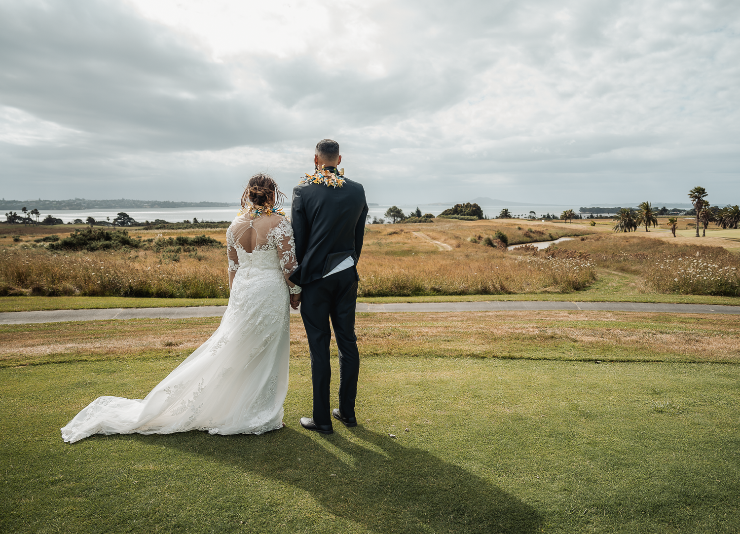 Wedding couple stands together on manicured golf course with ocean view.