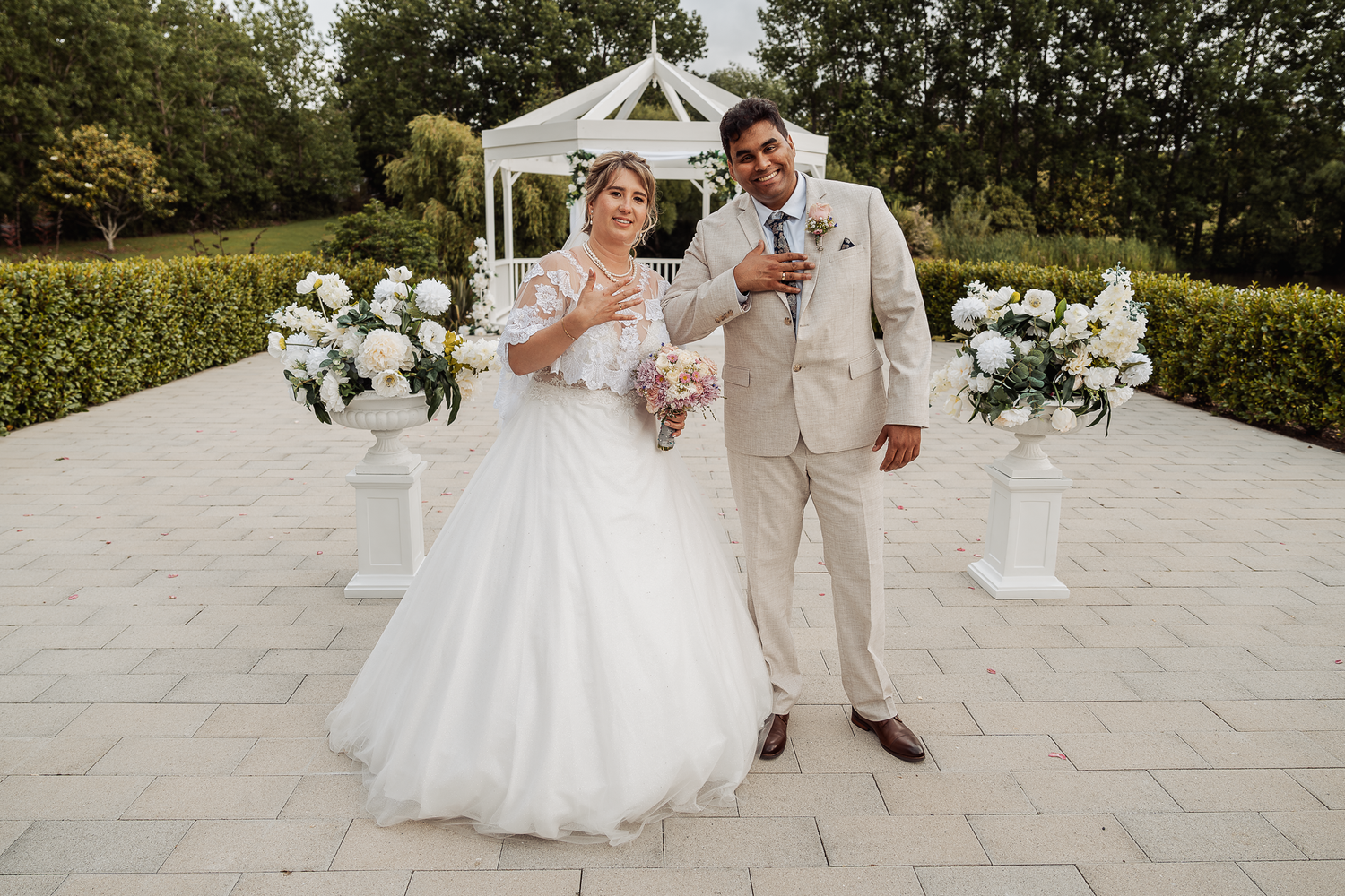 Newlyweds celebrate with champagne beneath a white gazebo decorated with floral arrangements.