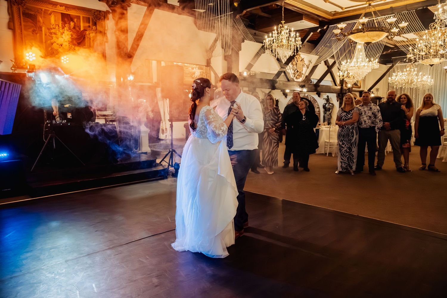 A couple in white attire dances together at a wedding reception with dramatic blue lighting effects.