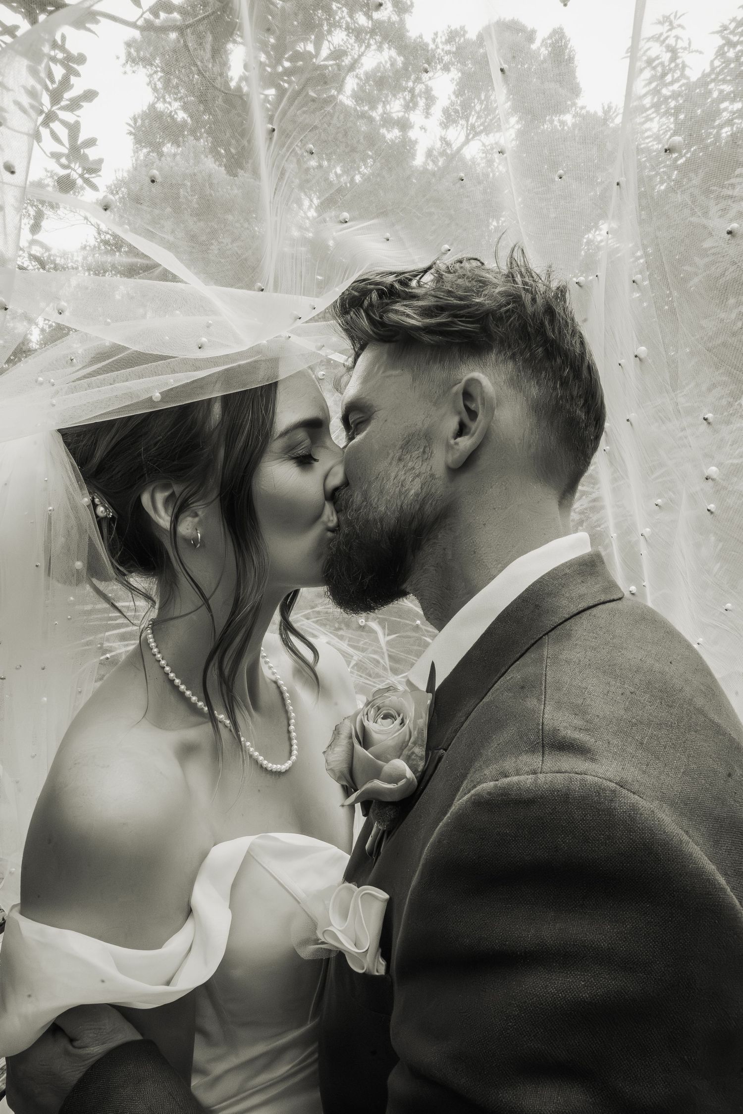 Black and white close-up of bride and groom sharing a kiss under the wedding veil.