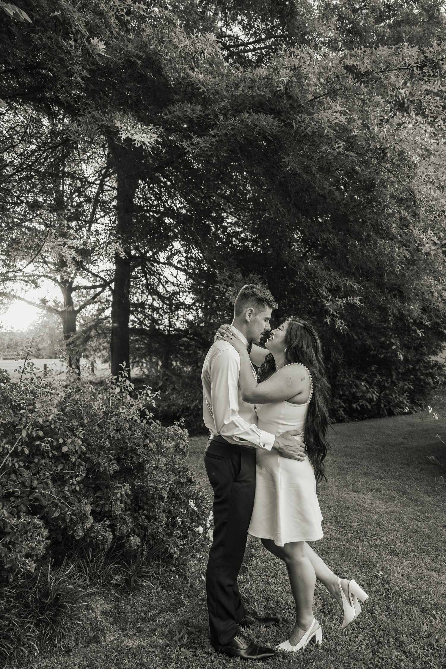 Black and white photo of couple embracing and kissing in garden on their wedding day.