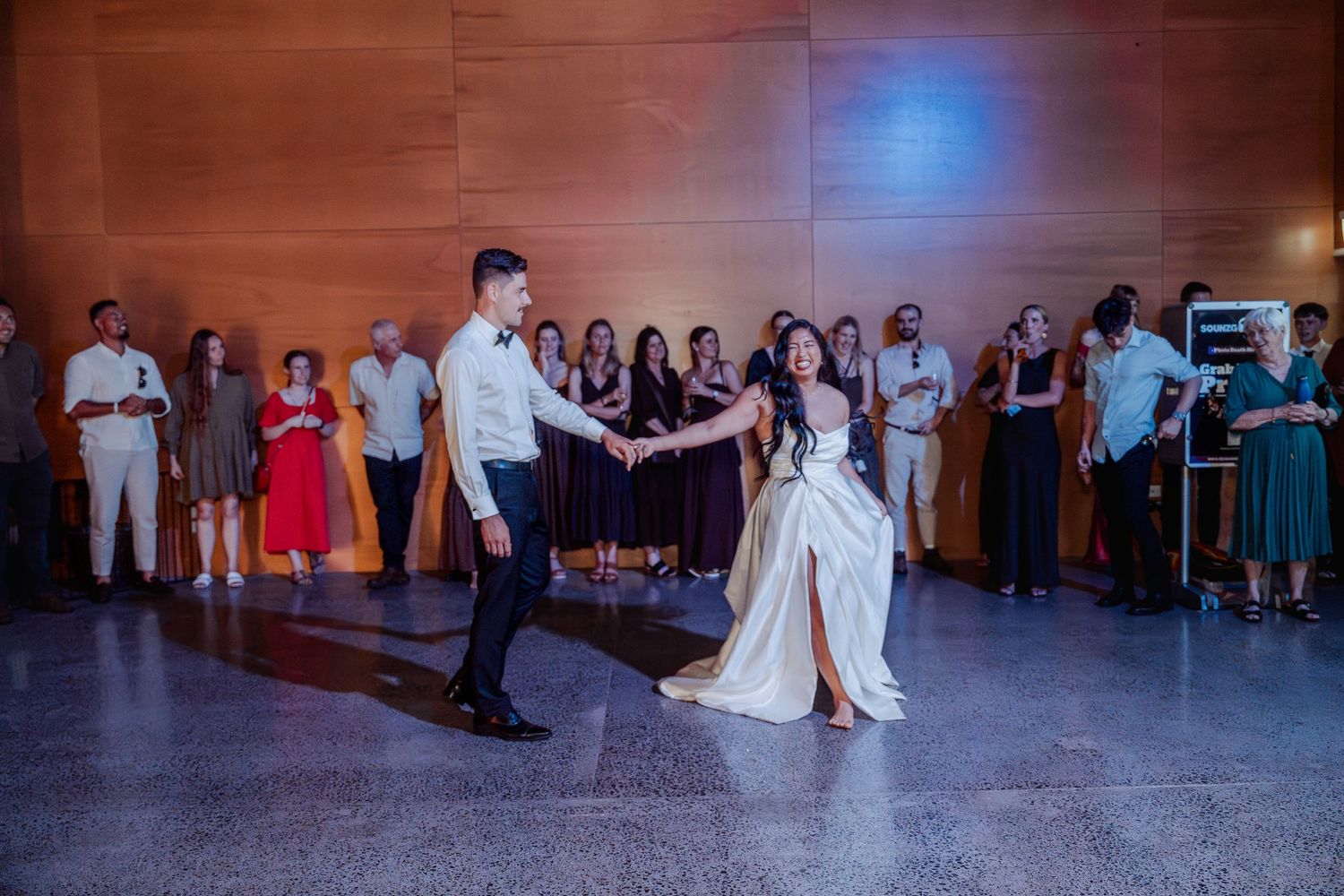 Bride and groom share their first dance at wedding reception while guests watch in elegant venue.