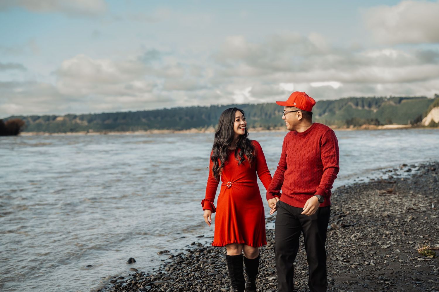 Couple in red outfits holding hands and smiling while walking along a rocky beach.