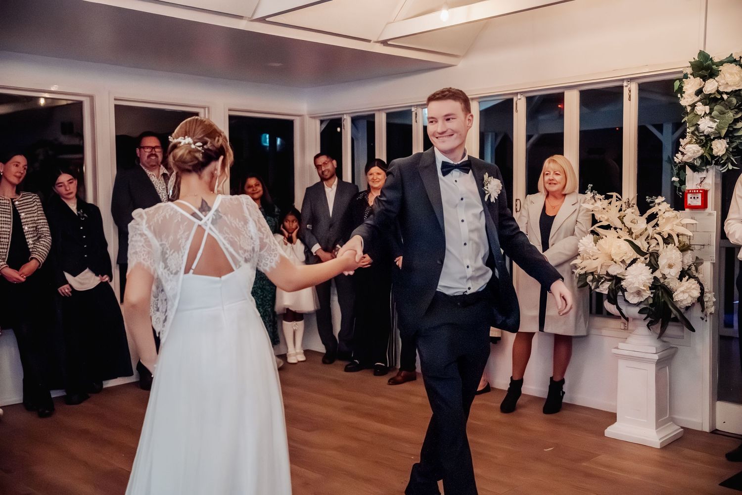 Wedding reception dance celebration in an elegant white-decorated indoor venue with hardwood floors.