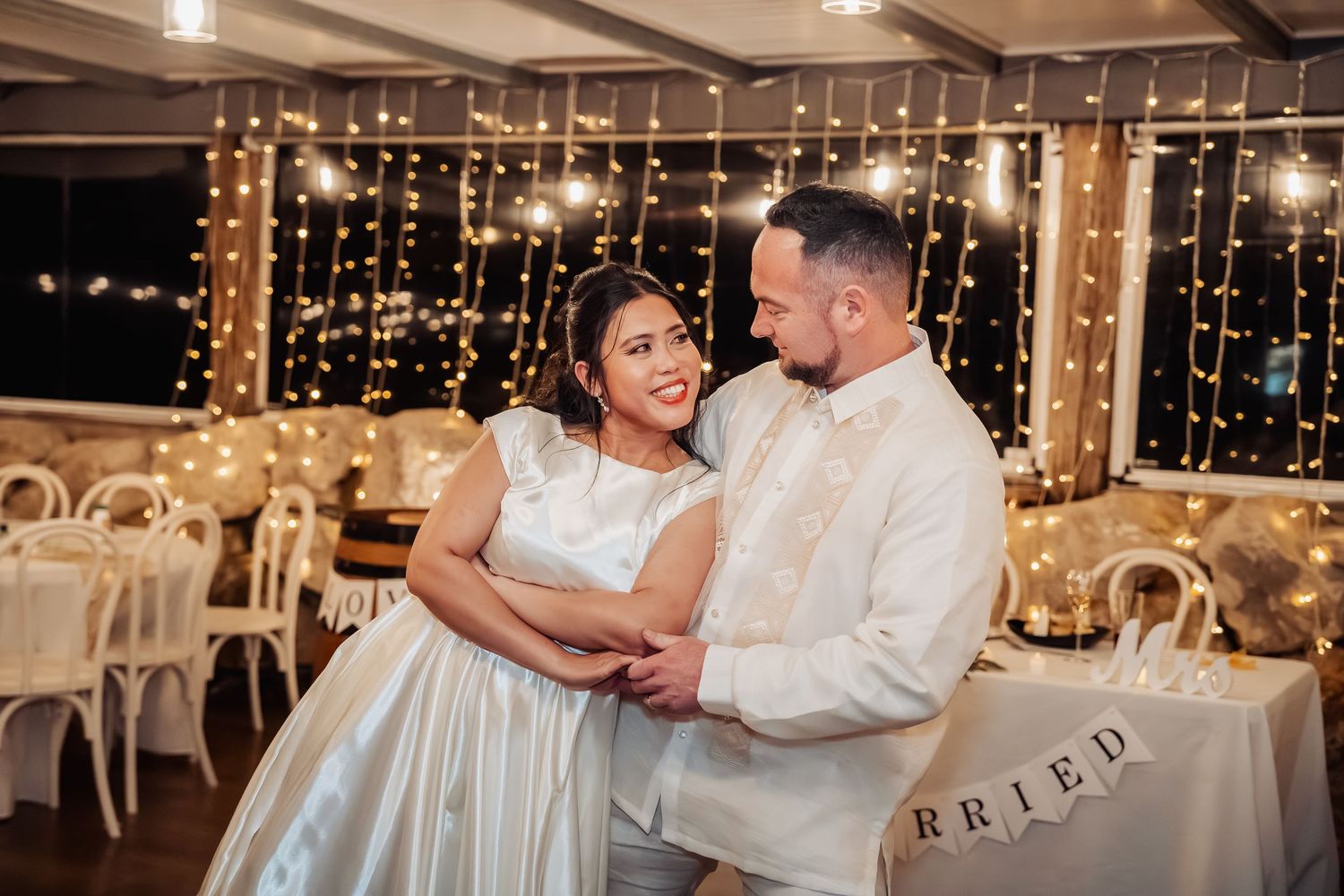 Wedding reception venue decorated with romantic string lights and white chairs for evening celebration.