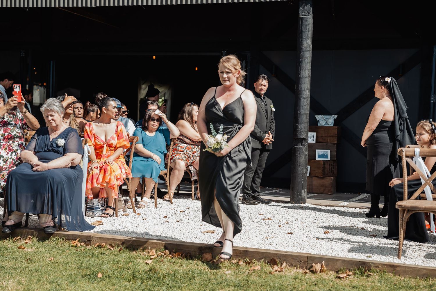 A person walks energetically during an outdoor celebration while guests watch from seating areas on a sunny day.