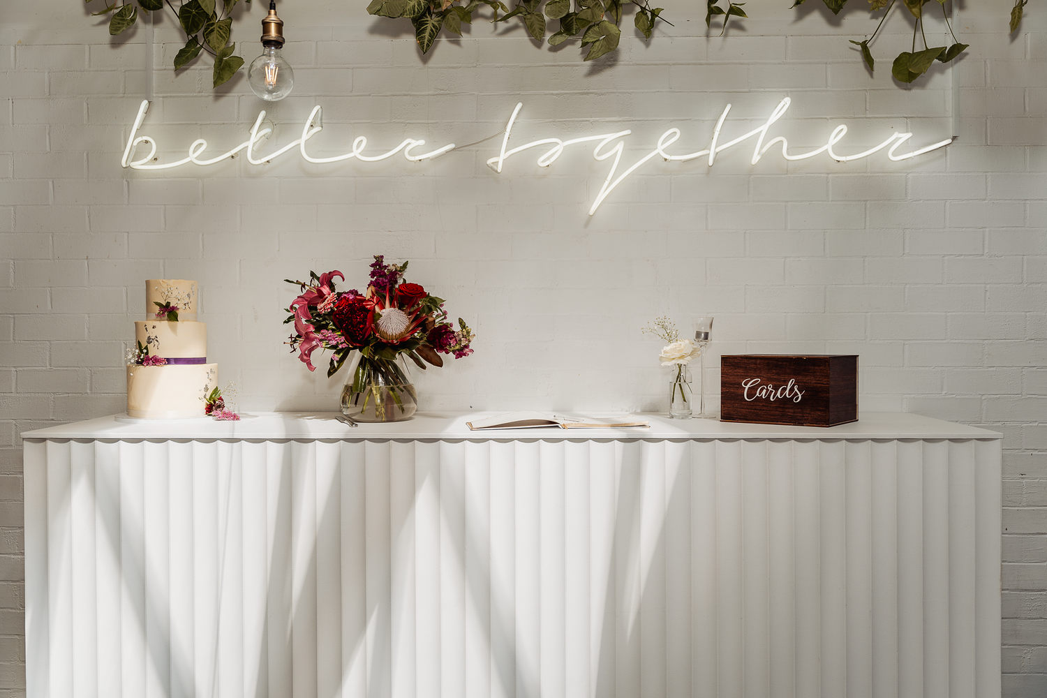 Wedding dessert table with neon 'better together' sign and floral arrangements.