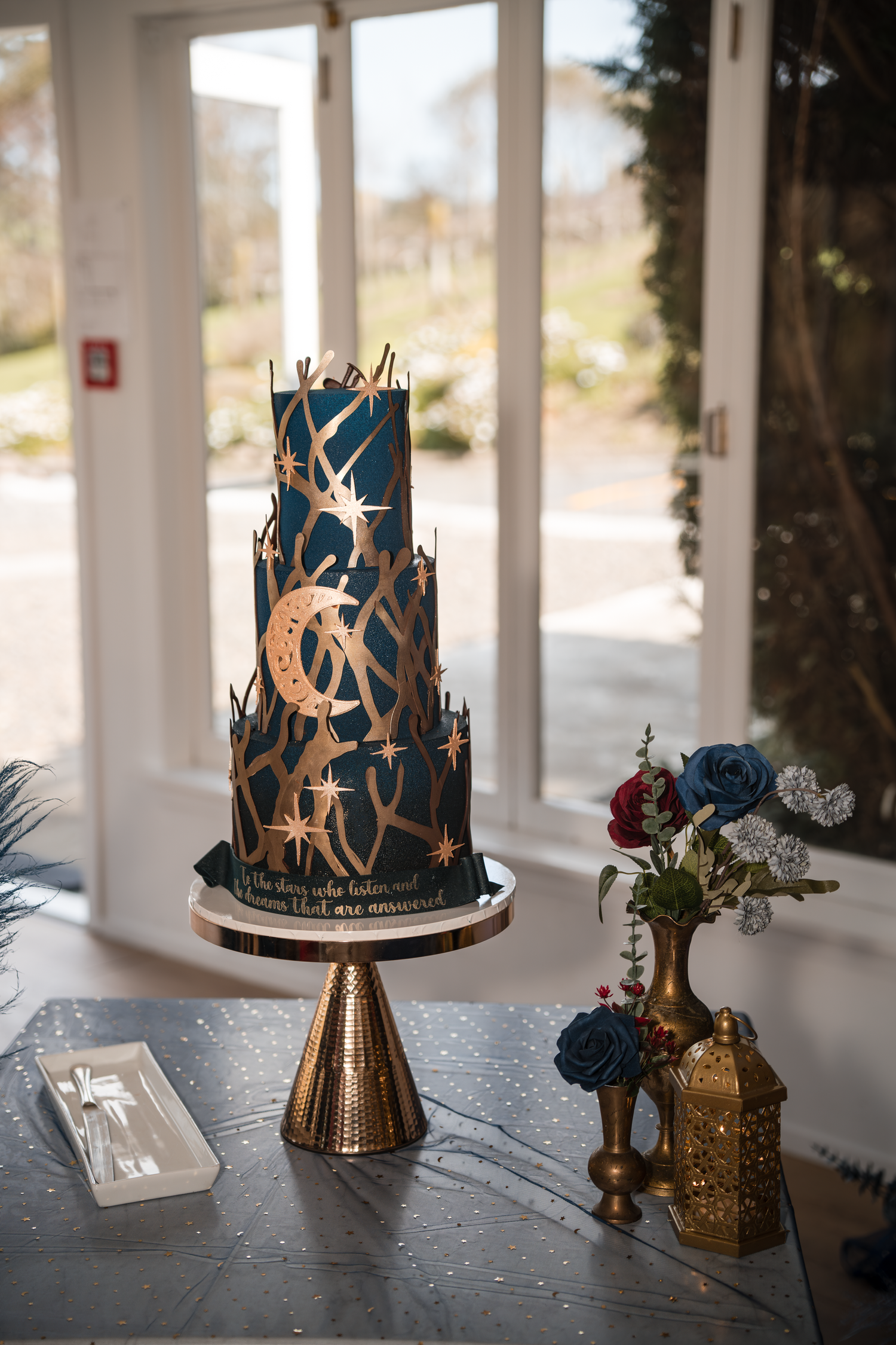 Modern three-tier navy and gold wedding cake displayed on a metallic stand with floral decorations.