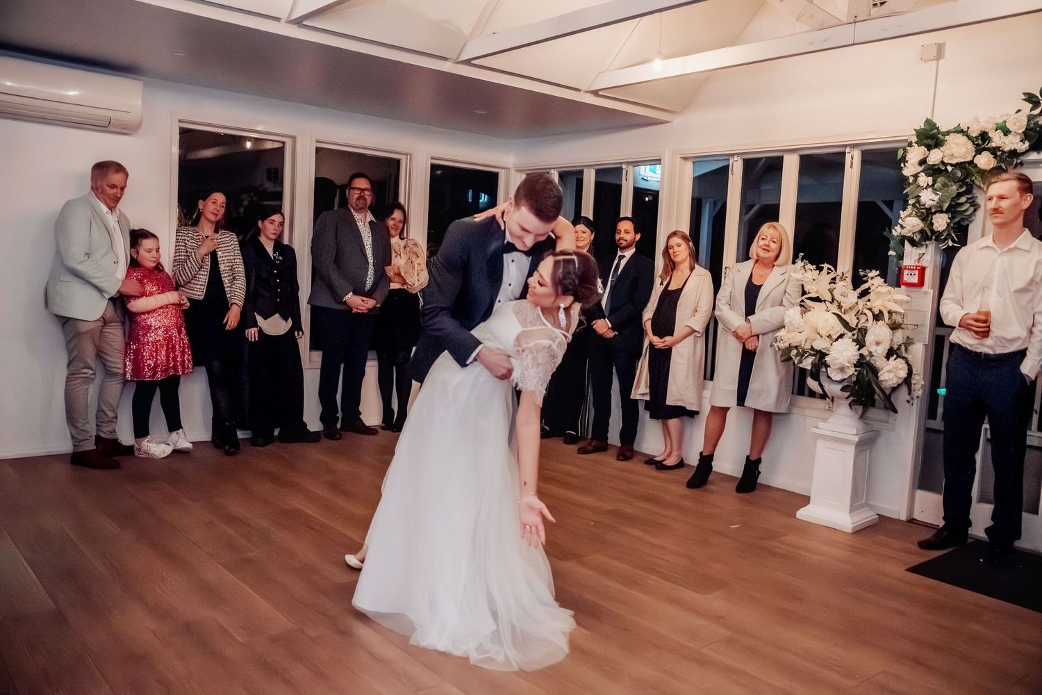 Wedding reception dance floor with guests gathered around in an indoor venue.