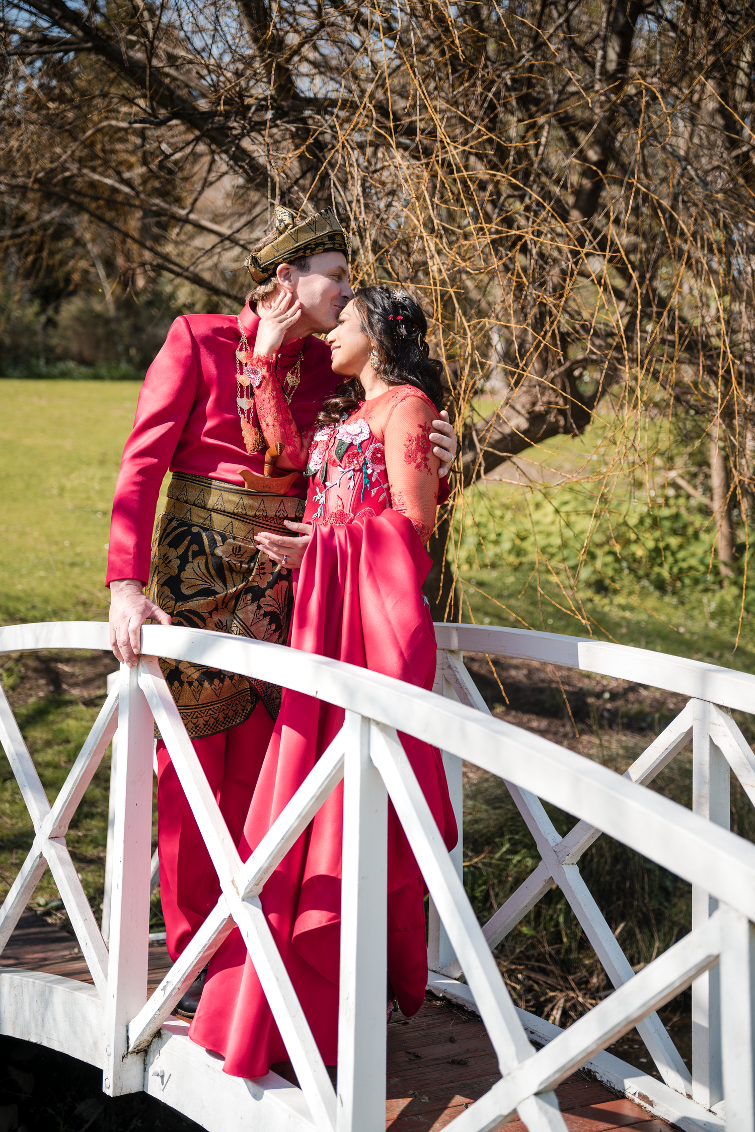Couple in matching pink attire sharing an intimate moment on a decorative white bridge.