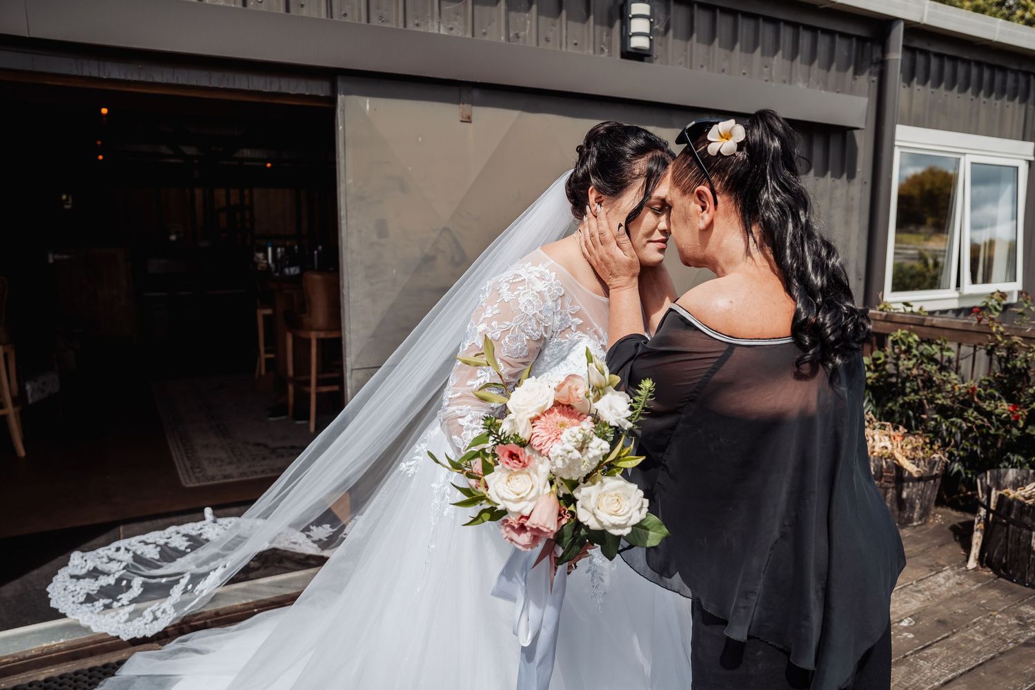 Two people share an emotional moment at a wedding celebration while holding a beautiful bouquet of blush and white roses.