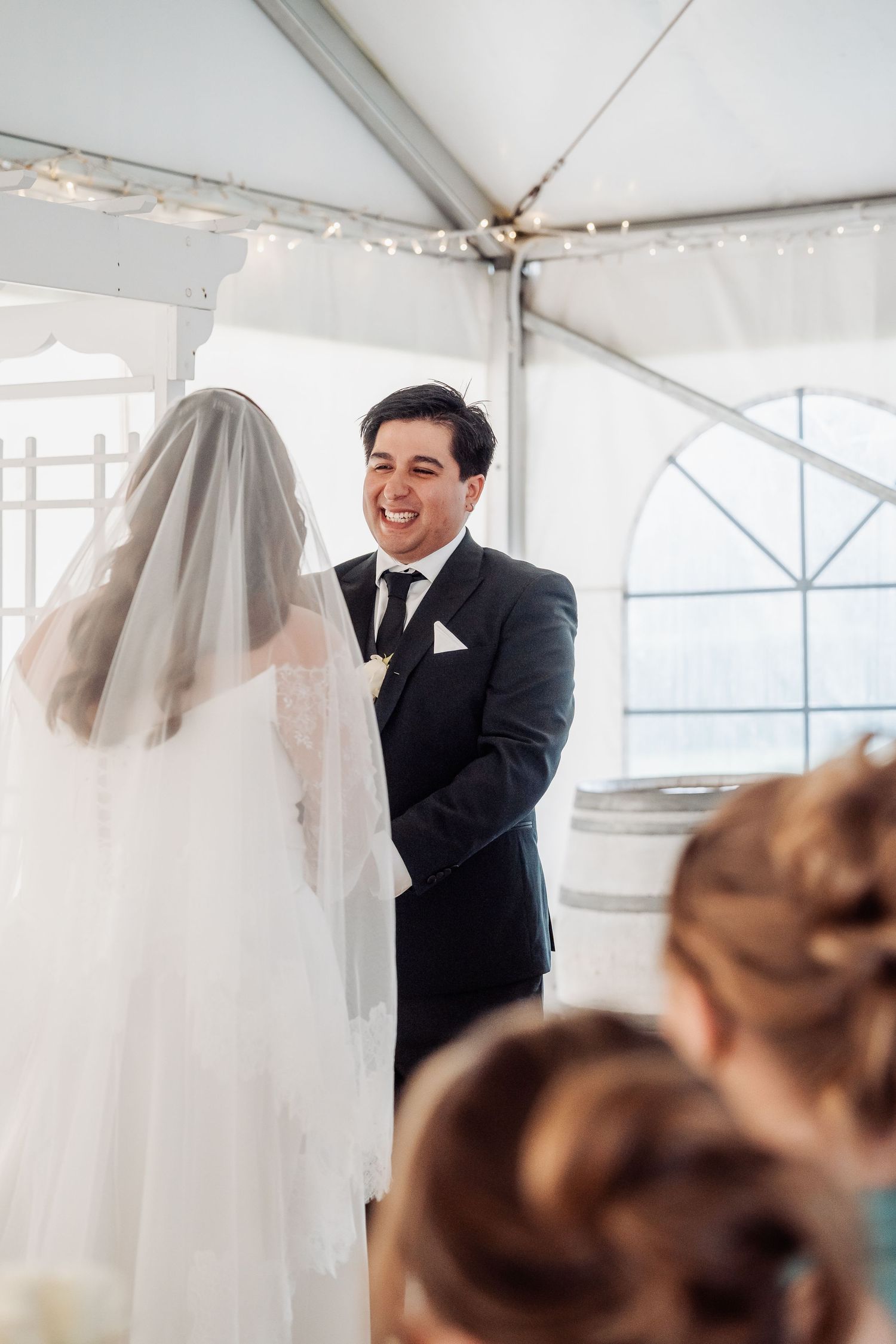 A joyful moment during a wedding ceremony under a white tent as the couple shares smiles at the altar.