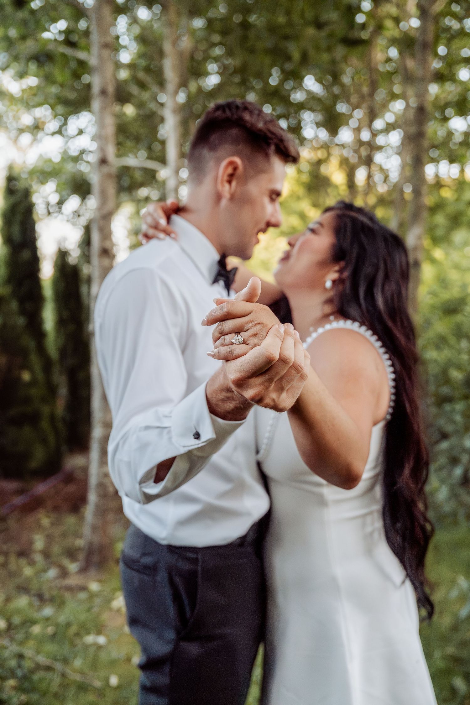 Bride and groom dance together holding hands in a beautiful outdoor garden setting.