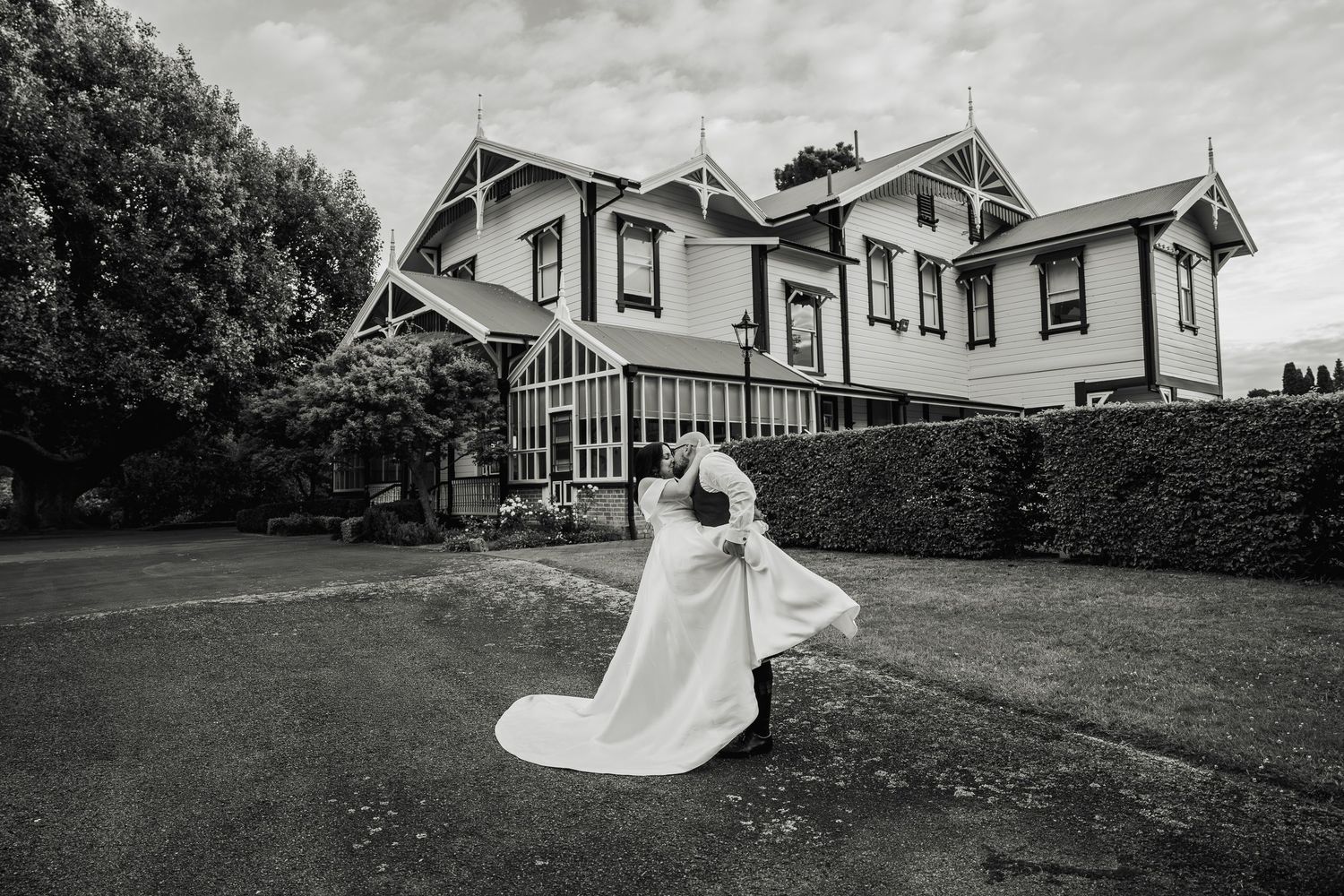 Black and white photo of groom lifting bride outside a grand Victorian wedding venue.