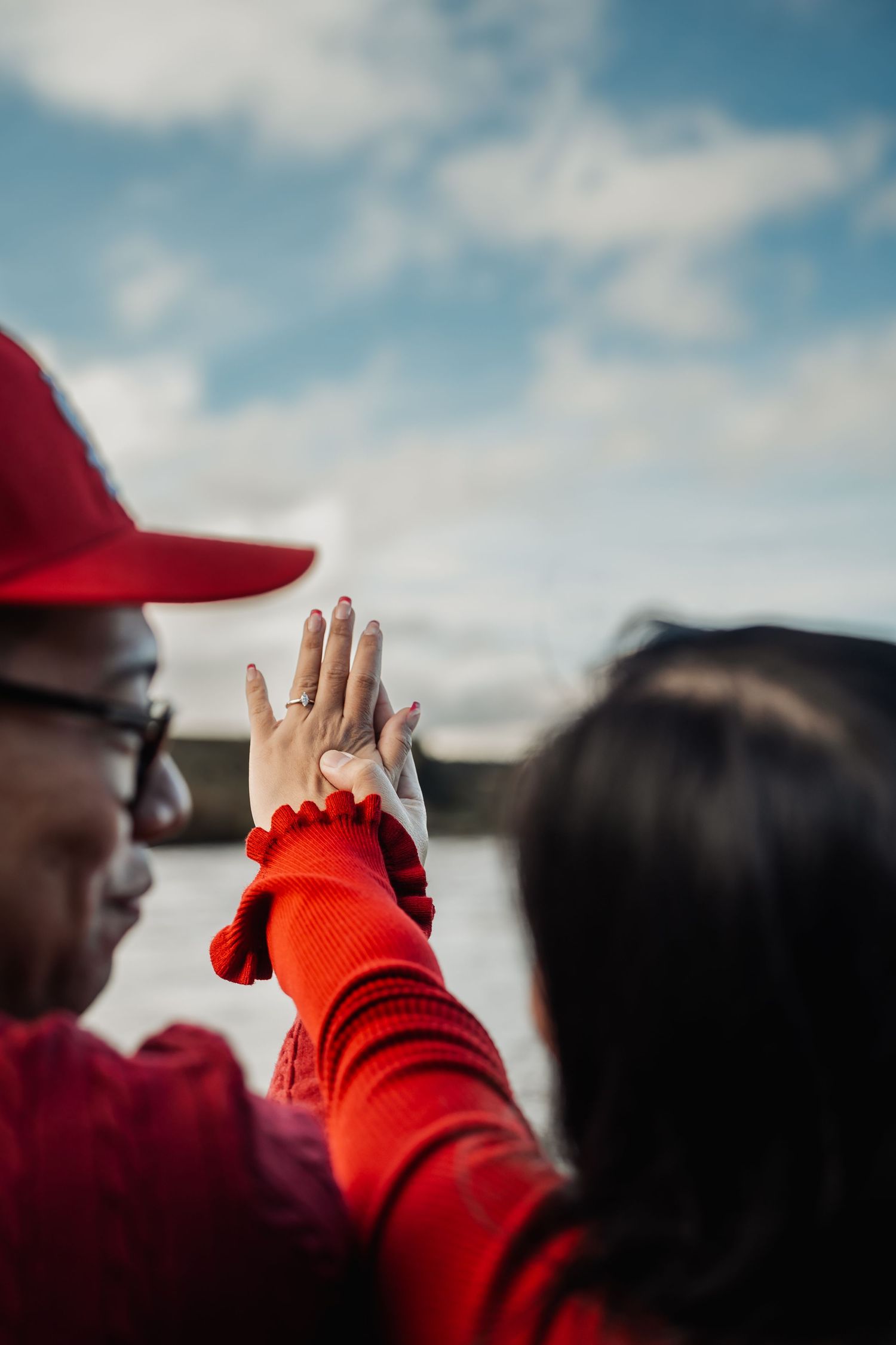 Close-up of couple in red outfits pressing palms together outdoors near a lake.
