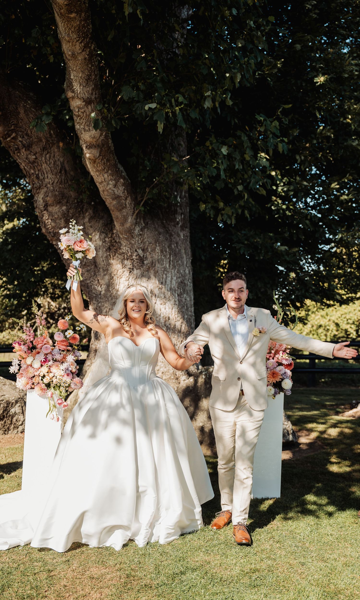 Joyful bride and groom celebrating after their outdoor wedding ceremony surrounded by pink floral arrangements.