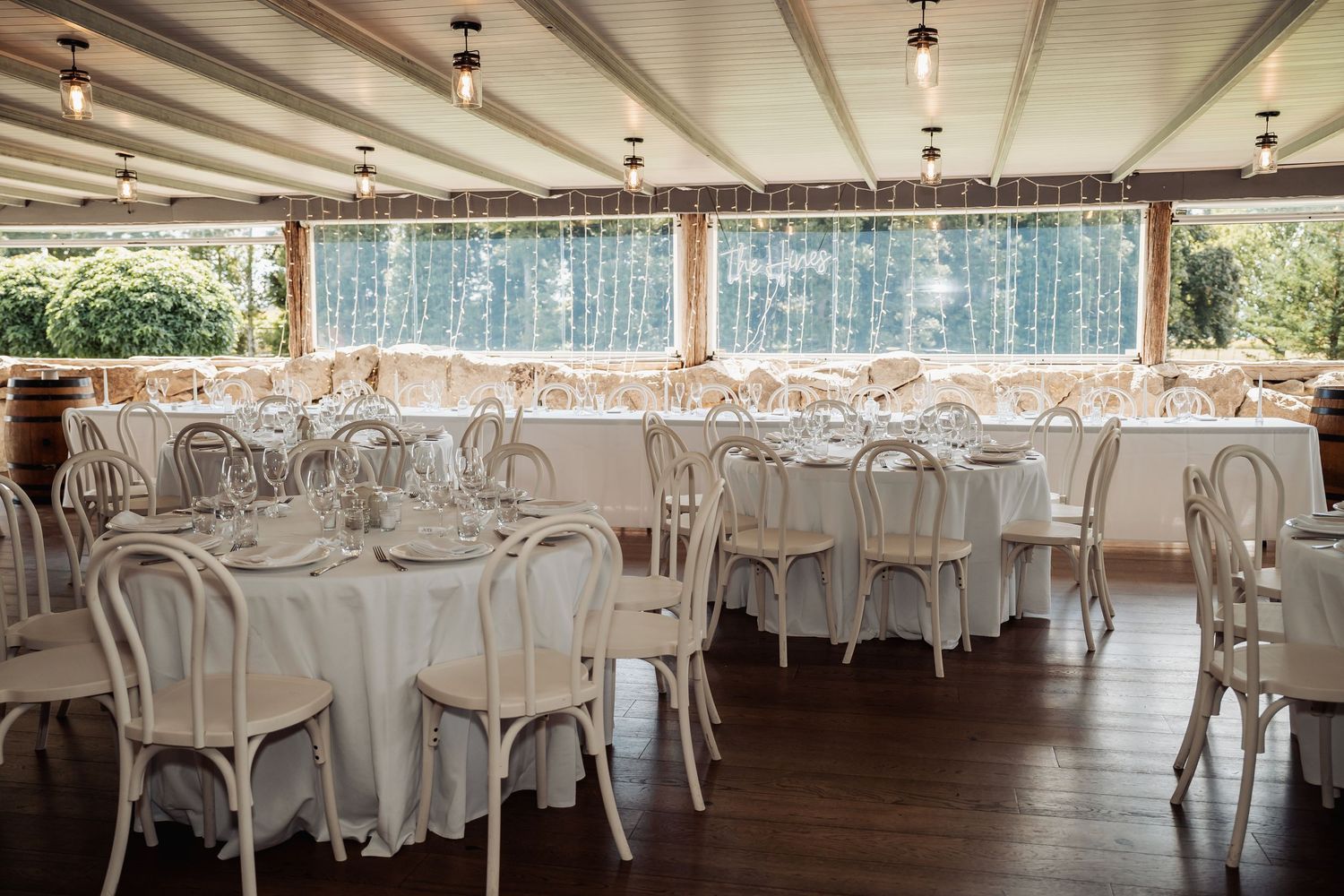 Elegant white wedding reception venue with round tables, white chairs, and fairy lights.