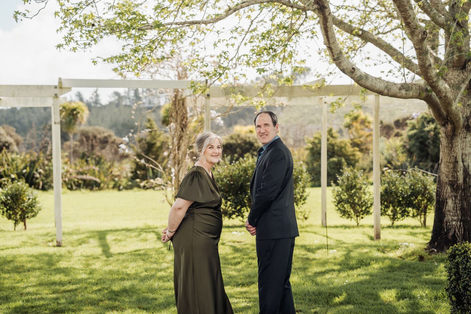 A couple stands together in an elegant outdoor garden setting during a special occasion.