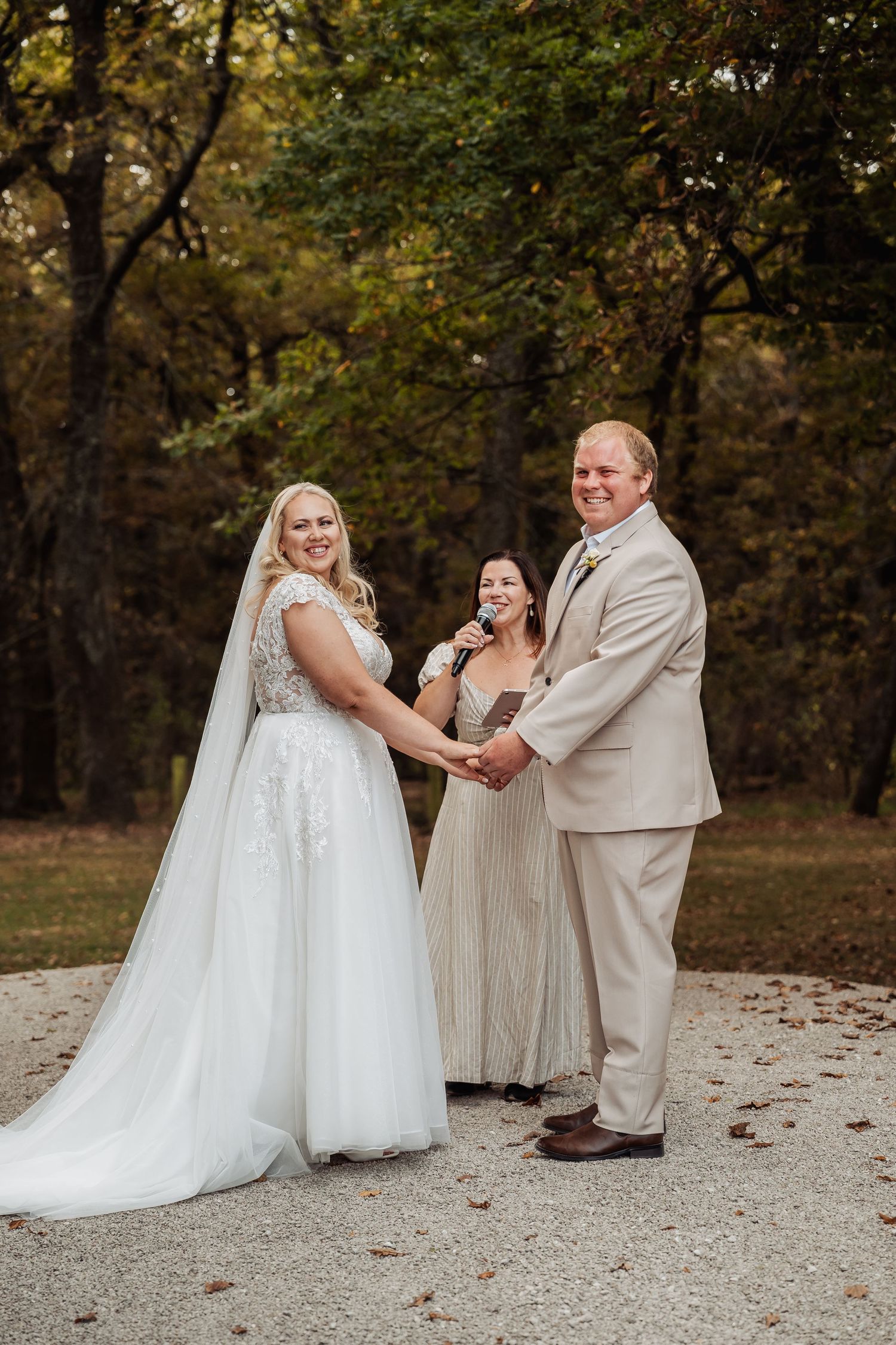 Bride and groom holding hands during outdoor fall wedding ceremony with officiant.