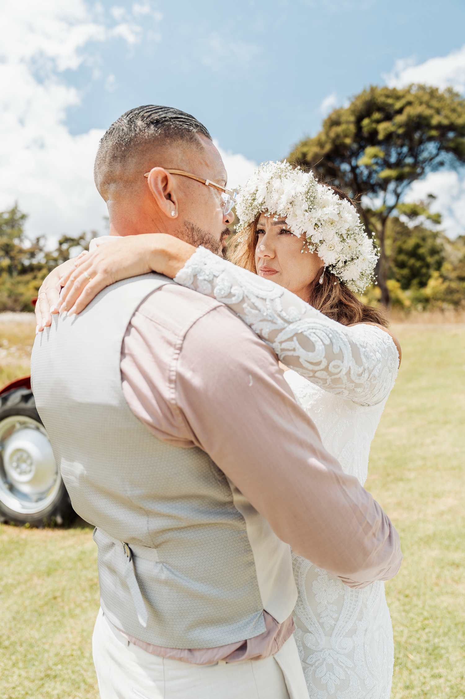Intimate embrace during outdoor wedding photoshoot with vintage tractor in background.