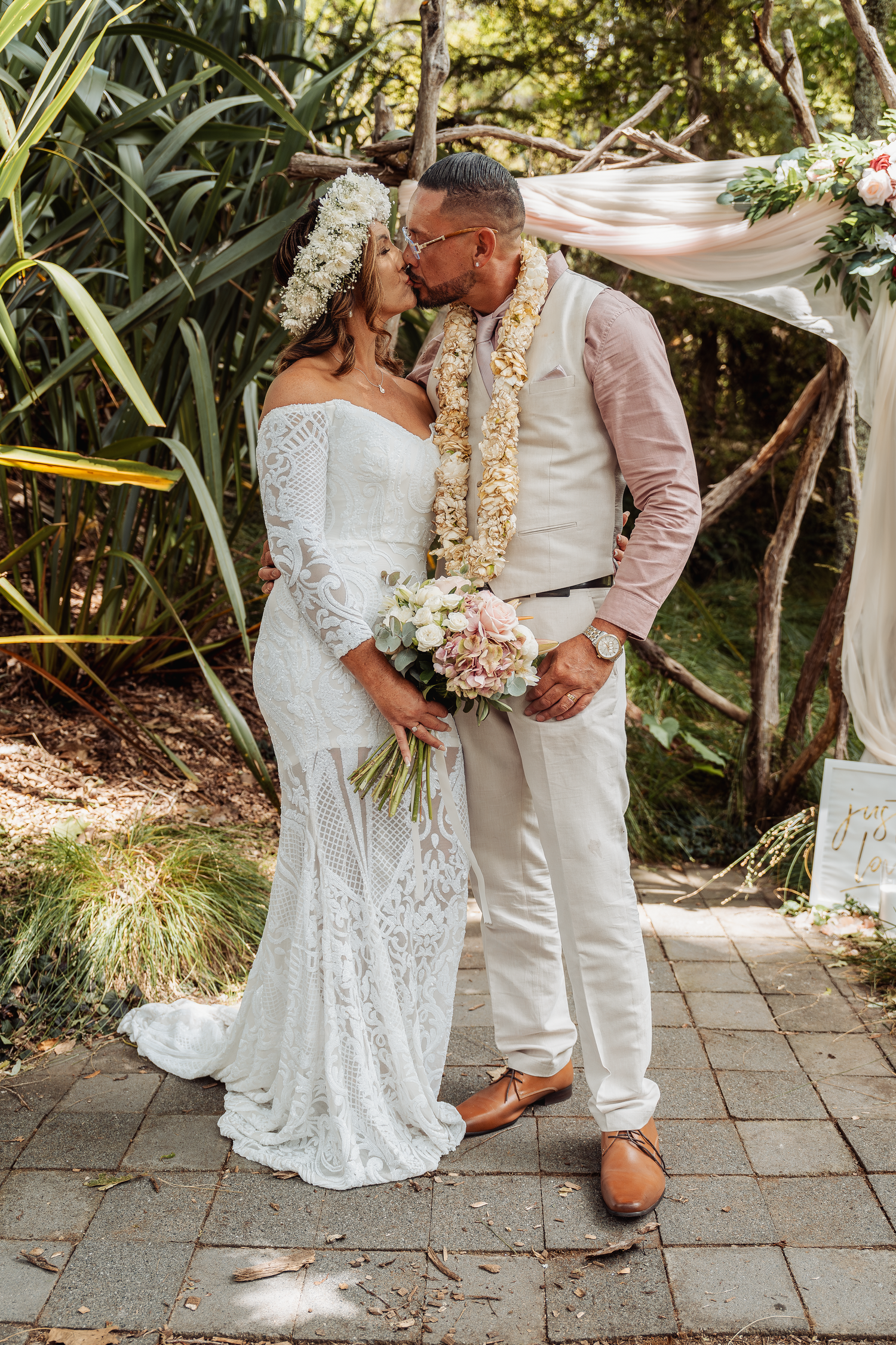 A romantic outdoor wedding ceremony under flowing white fabric with tropical greenery and floral decorations.