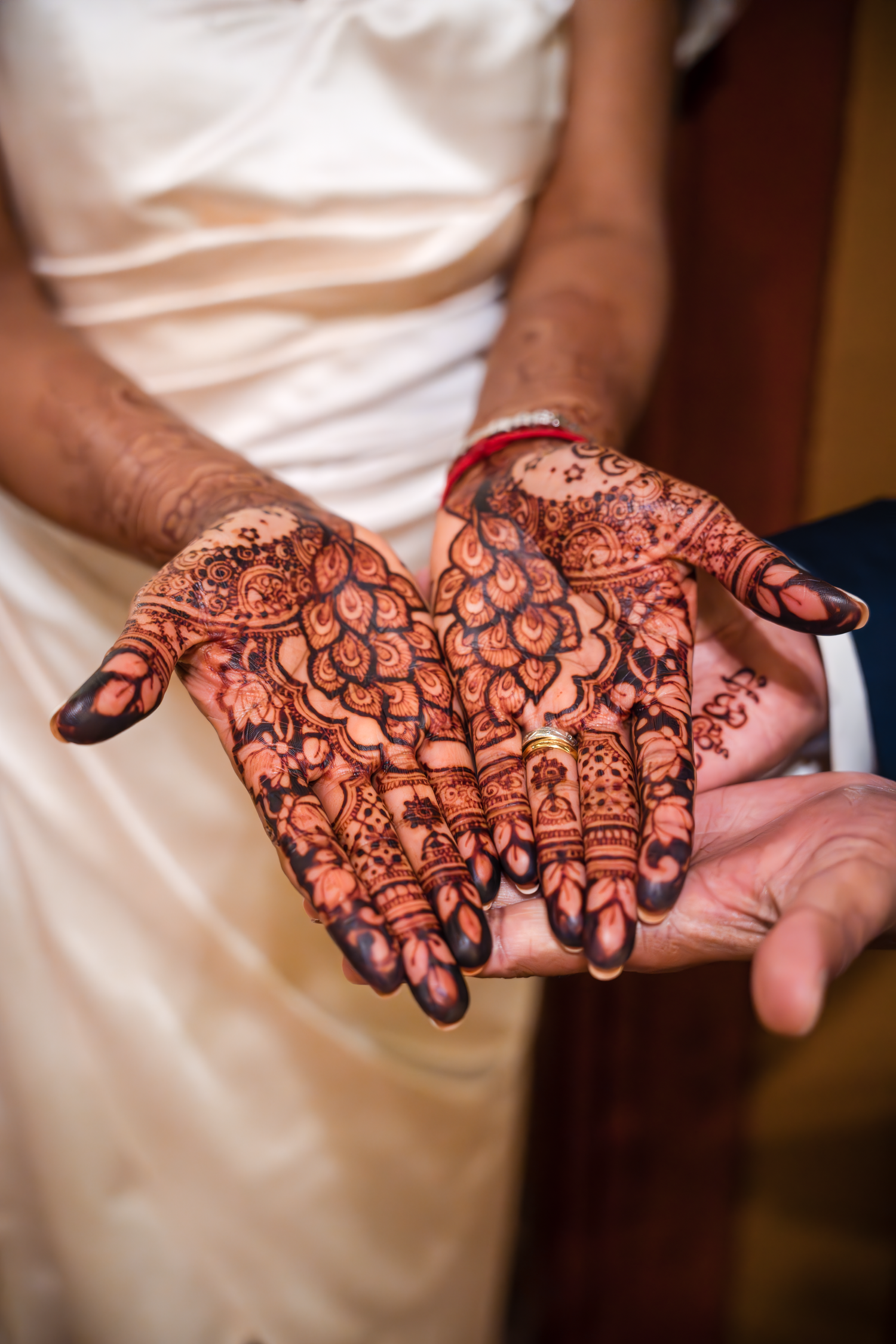 Detailed henna design displayed on palms with wedding dress in background.