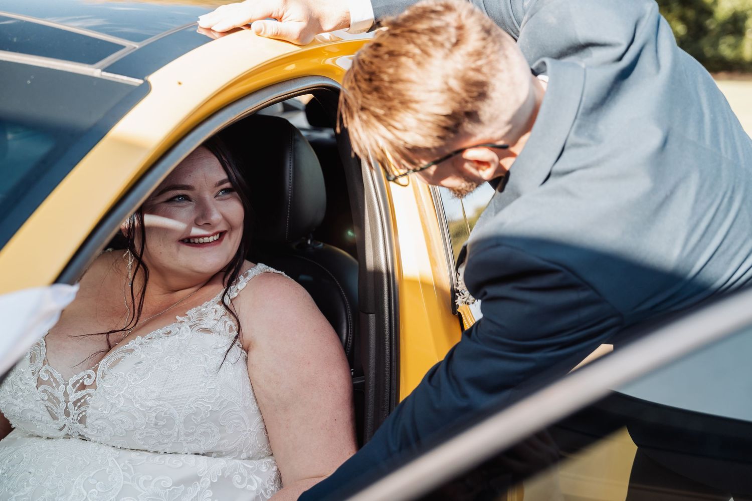 A candid moment of a bride sitting in a yellow car on her wedding day.