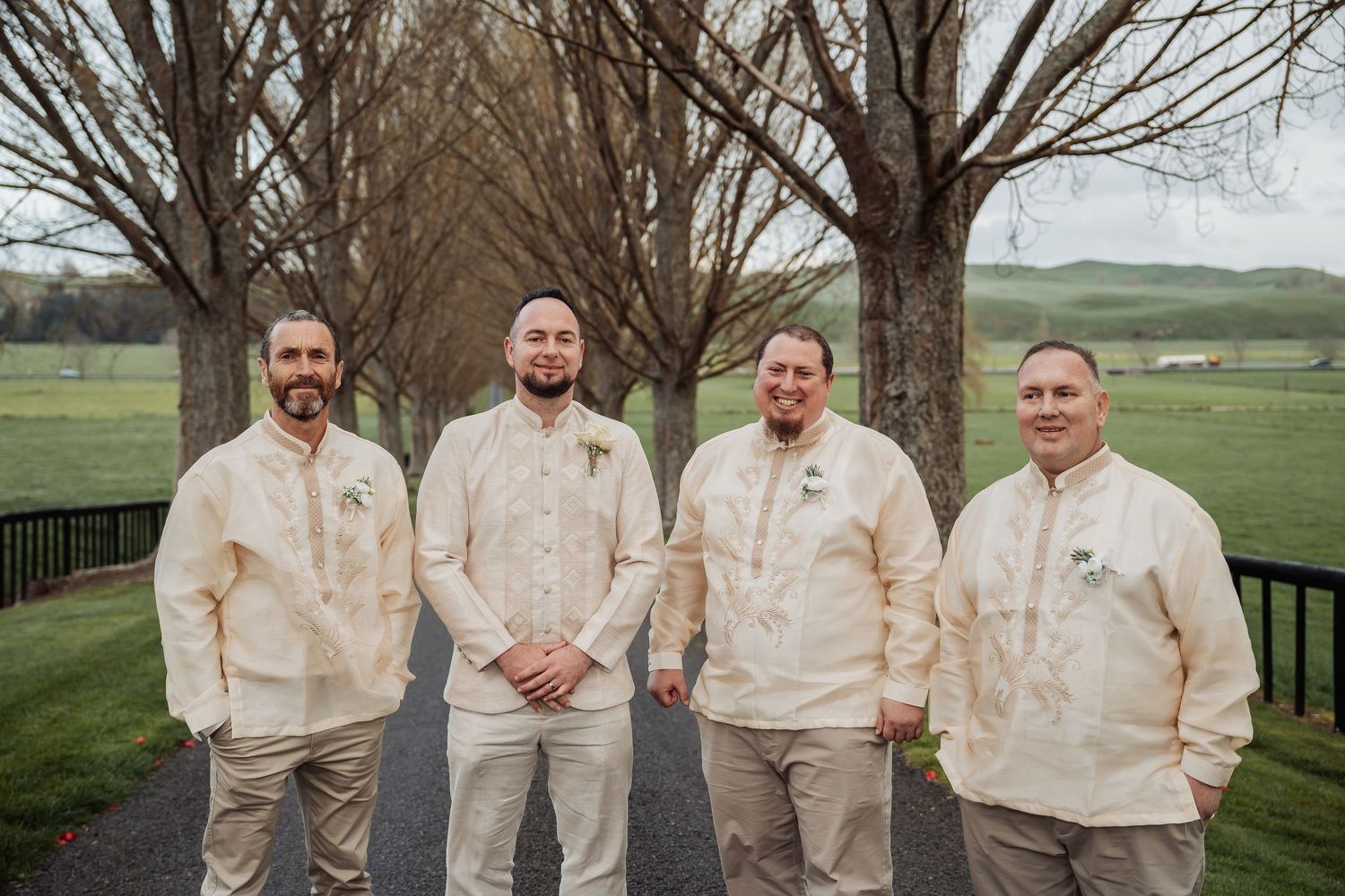 Wedding party in cream-colored attire posing outdoors against a scenic countryside backdrop.