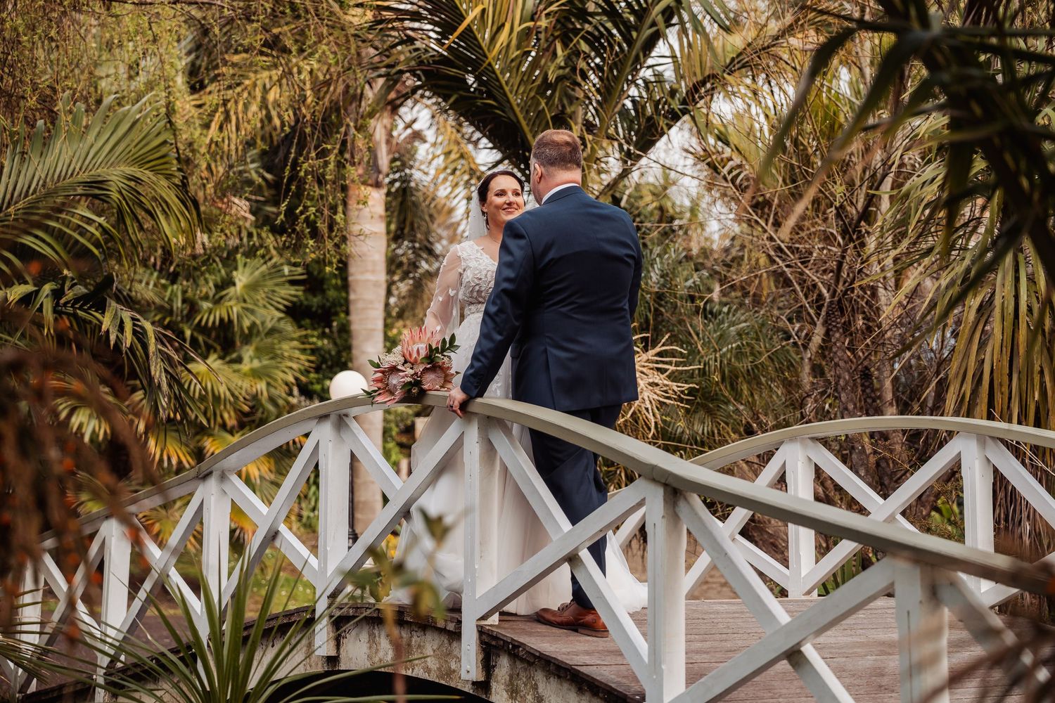 White wooden bridge walkway surrounded by tropical palm trees and landscaping.