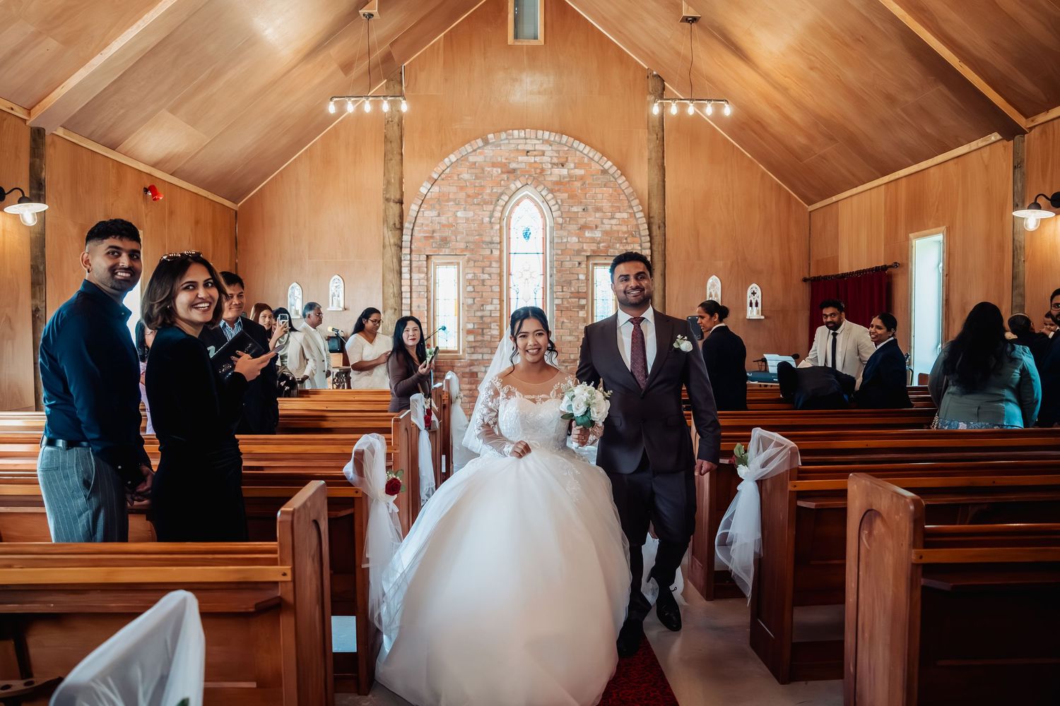 Newlyweds walking down the aisle of a charming wooden chapel surrounded by applauding guests.