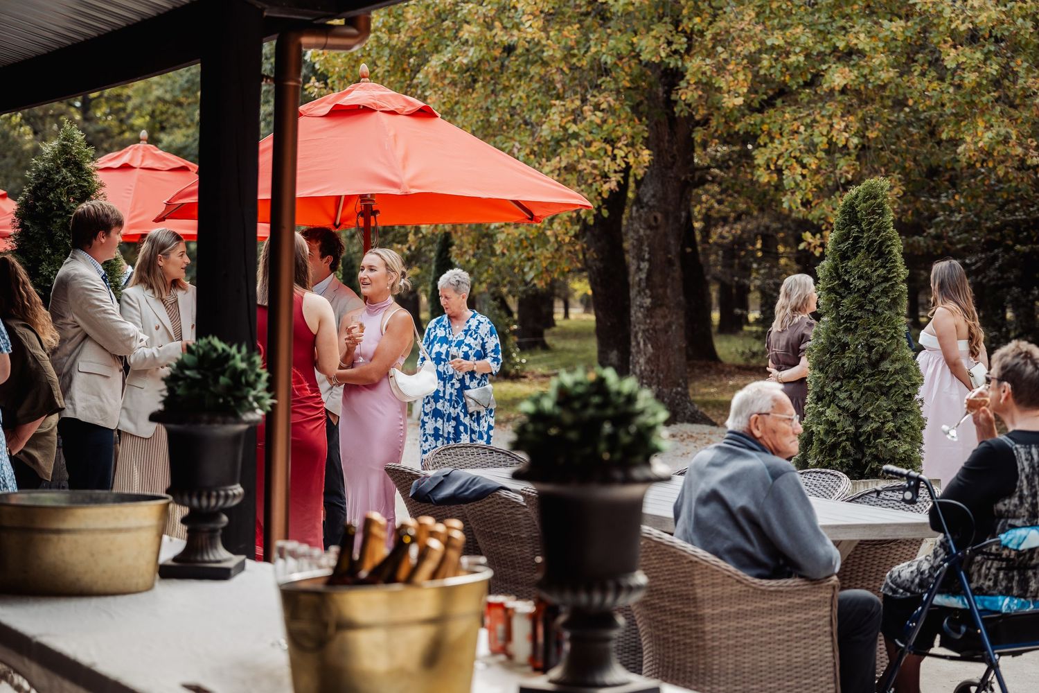 Guests mingle on an elegant outdoor patio with red umbrellas during a wedding reception.