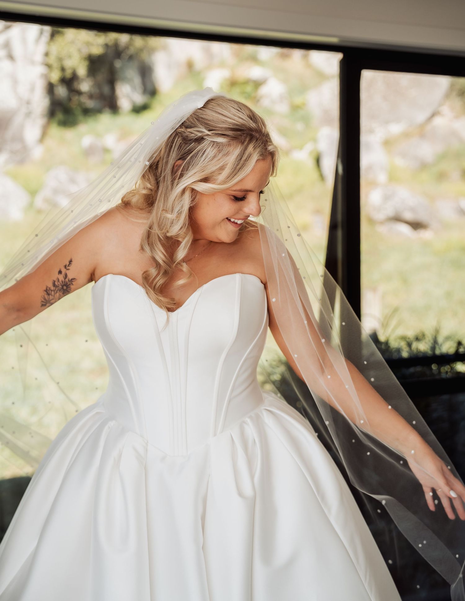 Blonde bride in strapless satin ballgown with pearl veil smiling on her wedding day.