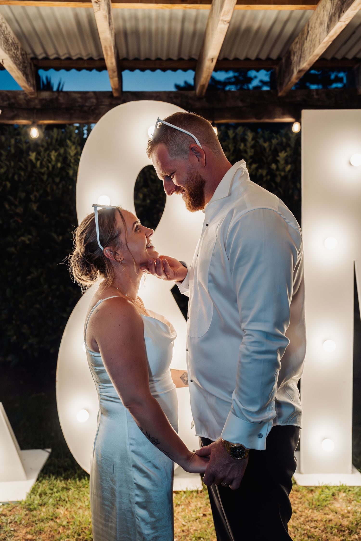 Couple shares a romantic moment holding hands in front of illuminated marquee letters at night.