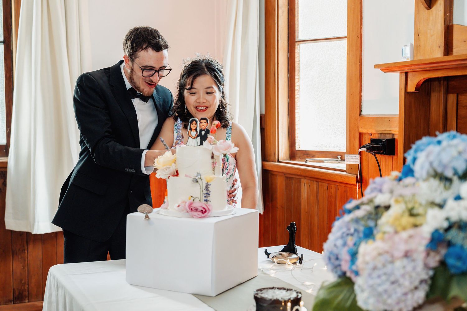Bride and groom cut their decorated white wedding cake at an elegant indoor reception.