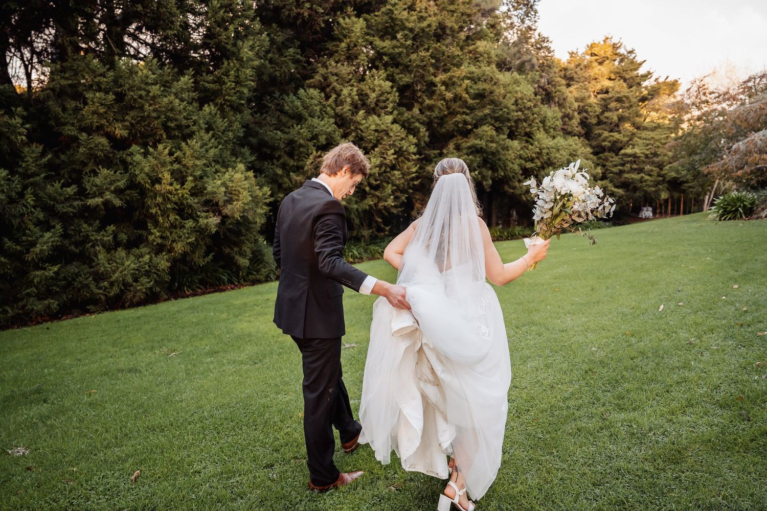 A couple walks together on a grassy hill during their romantic outdoor wedding ceremony on a fall afternoon.