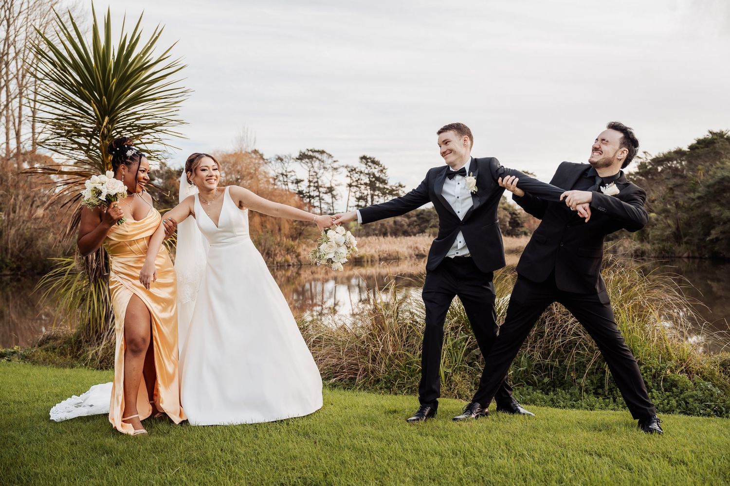 Wedding party posing playfully on grassy hillside in formal attire.