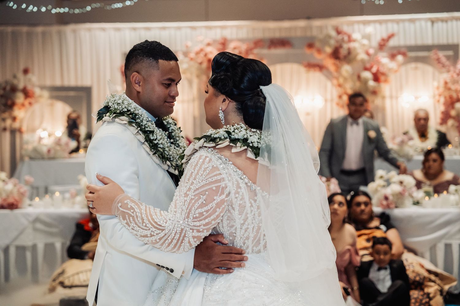 Couple sharing intimate dance at wedding reception with decorative lighting and floral arrangements.