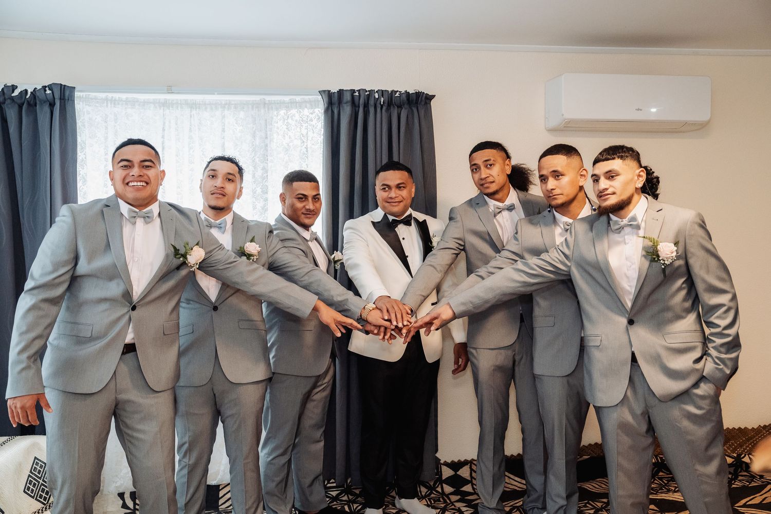 Groomsmen in matching gray suits pose together for wedding party photos in a bright indoor venue.