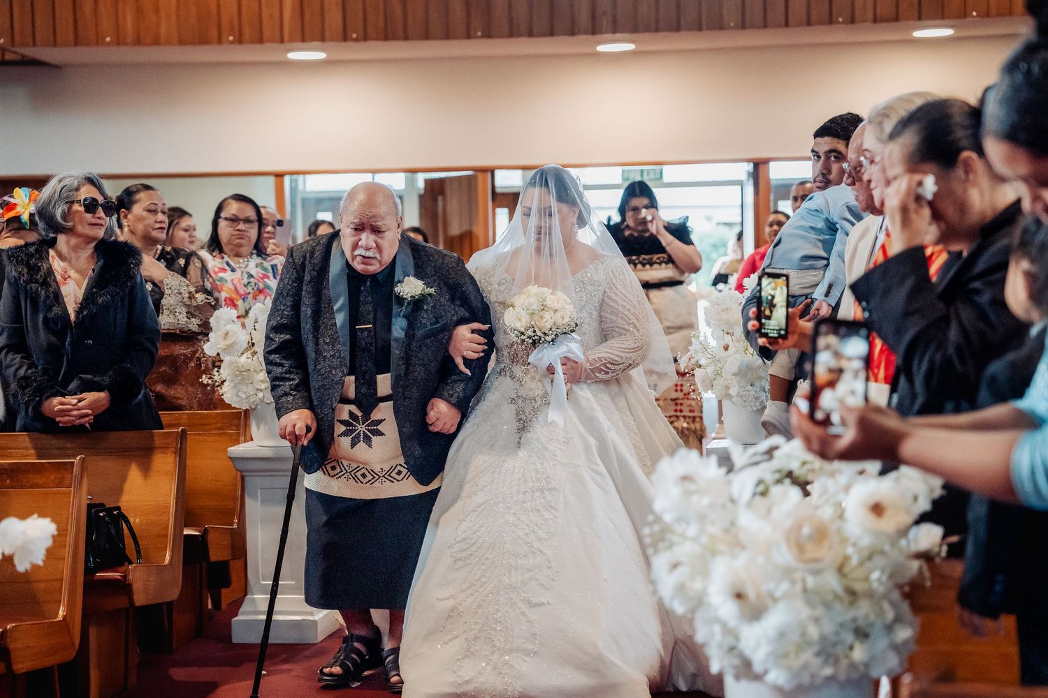 Elegant church interior decorated with white floral arrangements and guests seated for wedding ceremony.