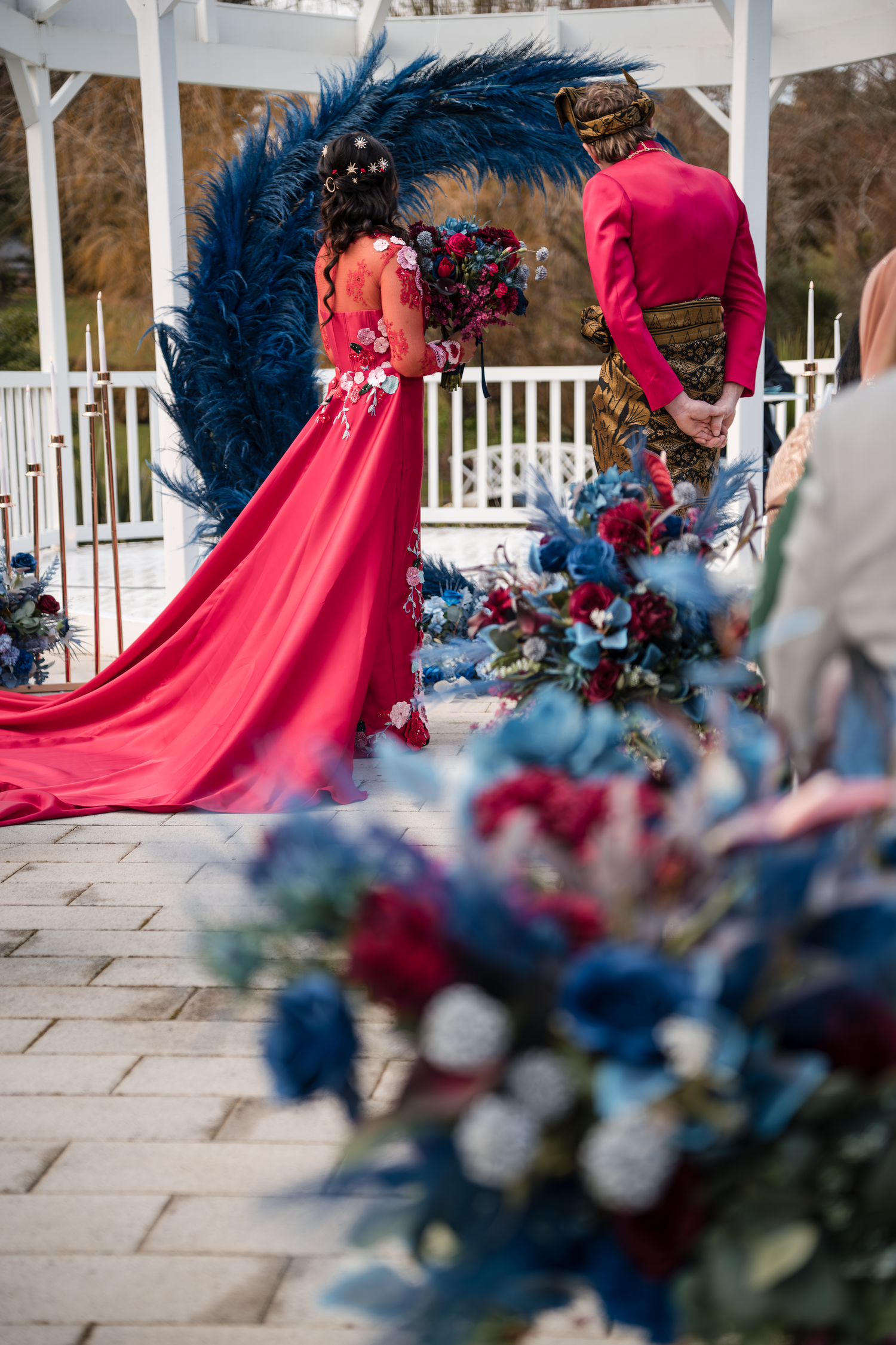 Dramatic red wedding dress with blue floral decorations against a white gazebo backdrop.