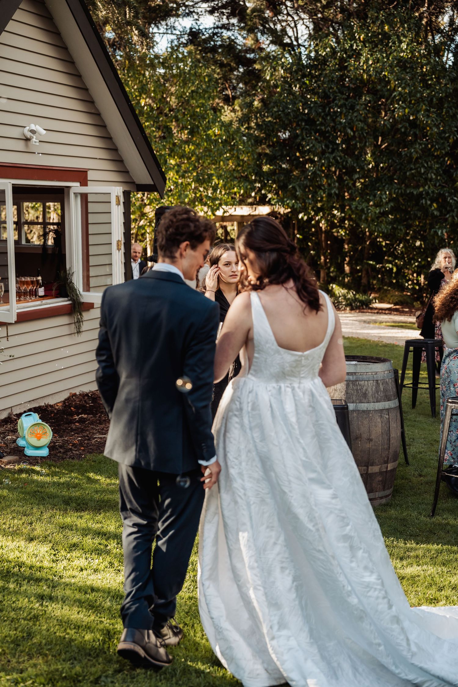 Bride and groom holding hands walking toward rustic venue building at golden hour.