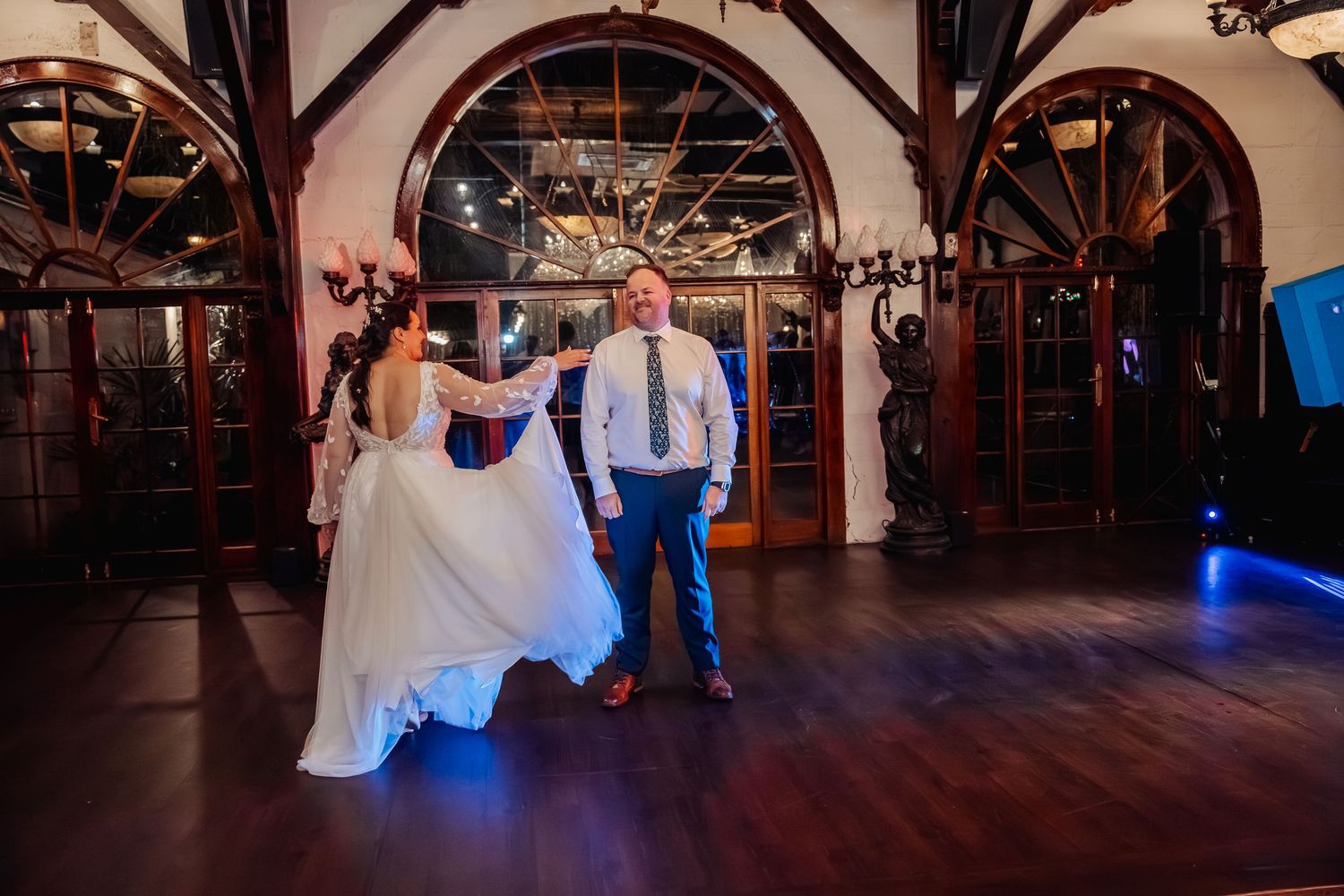 Wedding reception venue with vaulted ceilings, arched windows and dark wood dance floor.