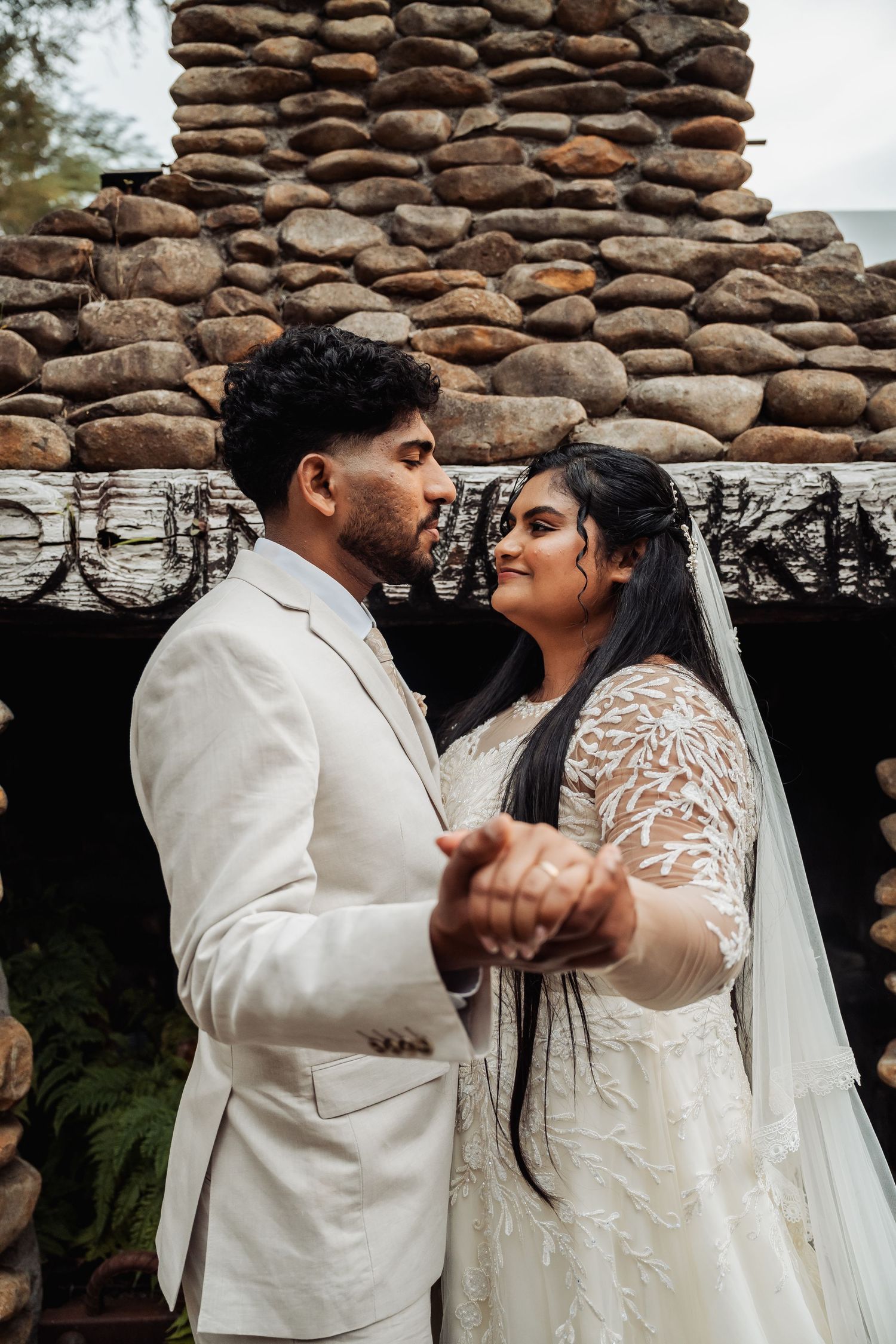 Bride and groom holding hands and dancing outdoors in front of a rustic stone wall.