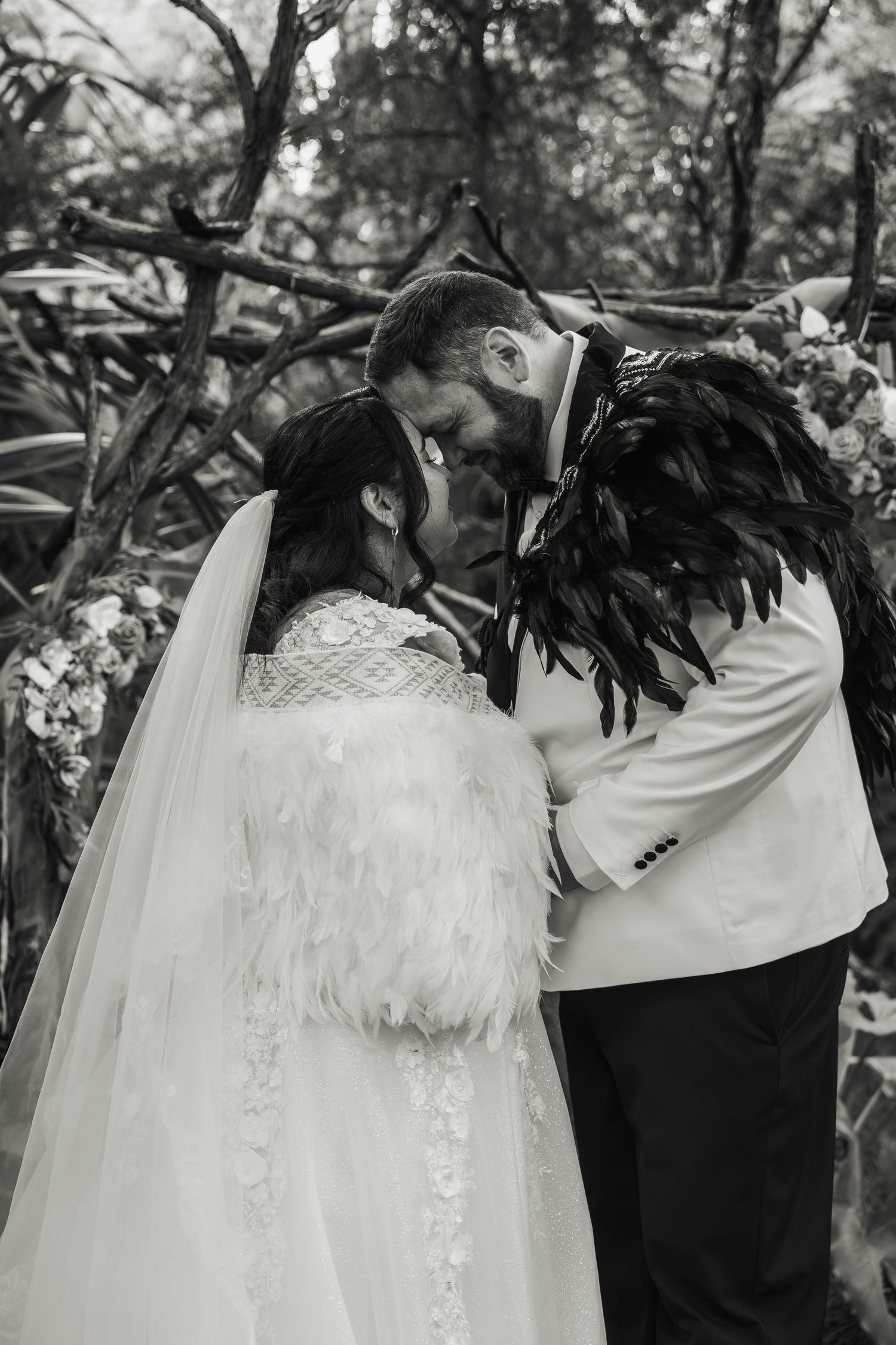 Black and white photo of bride and groom sharing first kiss at forest wedding altar.