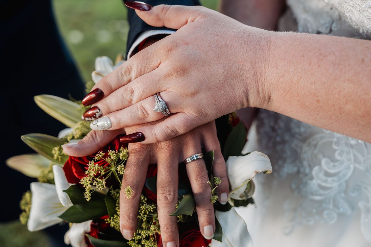 Close-up of wedding rings and hands resting on a floral bouquet with white lilies.