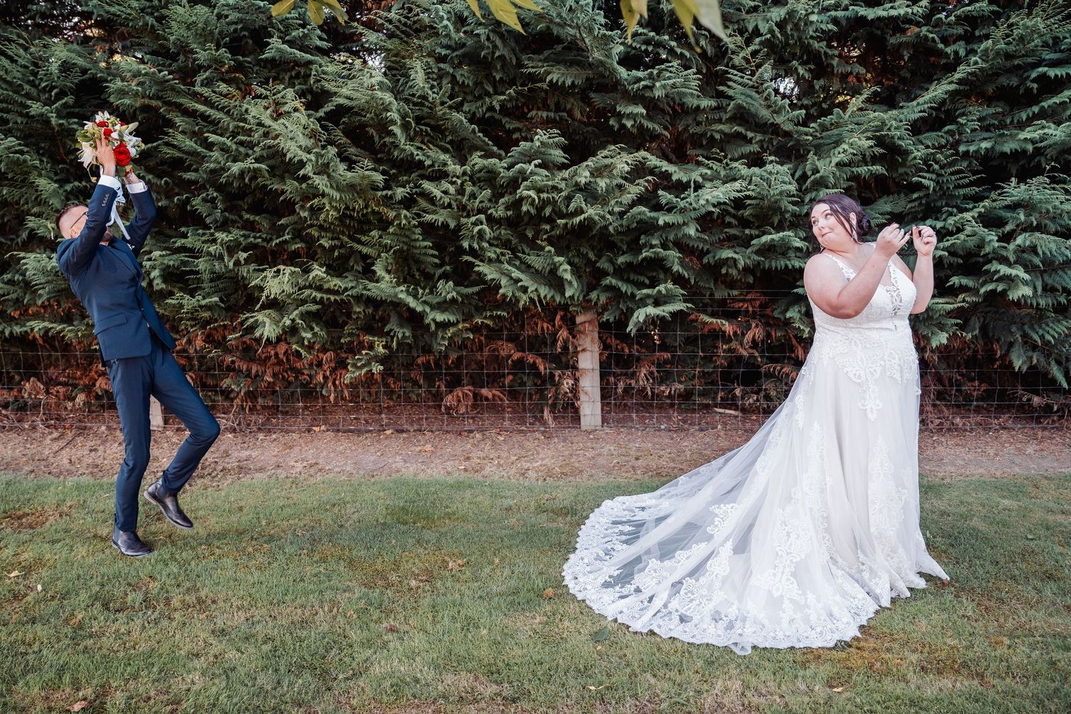 Playful wedding photo of a couple taking pictures of each other in a garden setting.