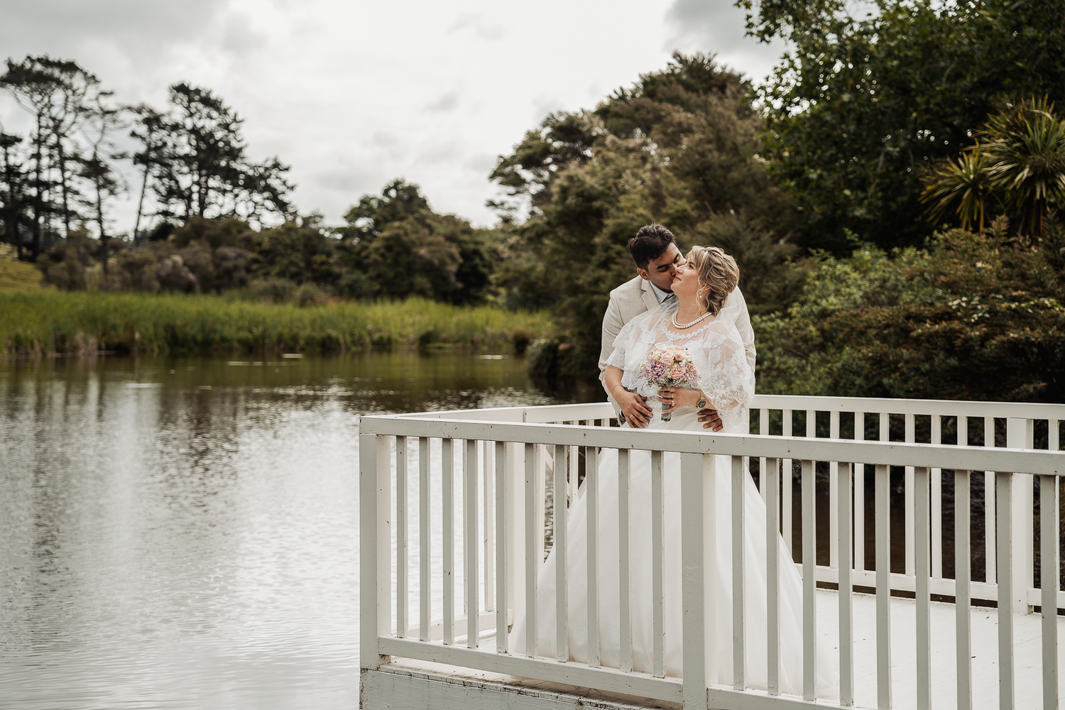 A romantic moment shared on a white bridge overlooking a serene pond.