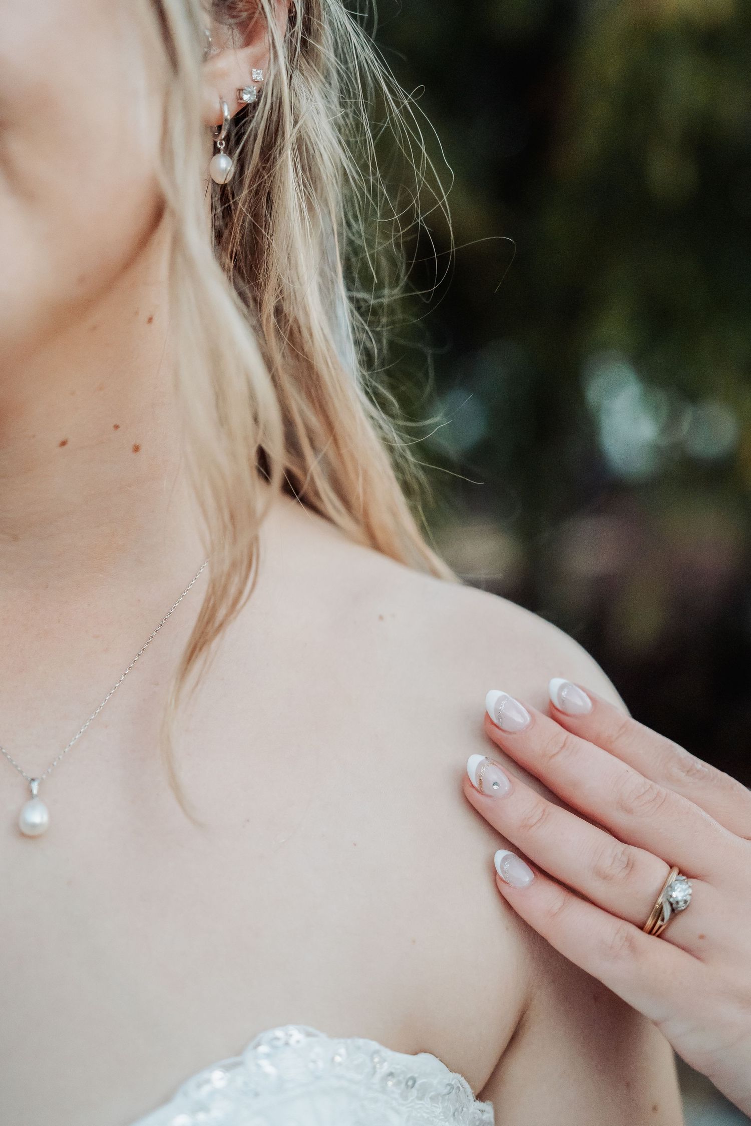 Close up of a bride wearing a white lace dress showing delicate jewelry and engagement ring on her manicured hand.