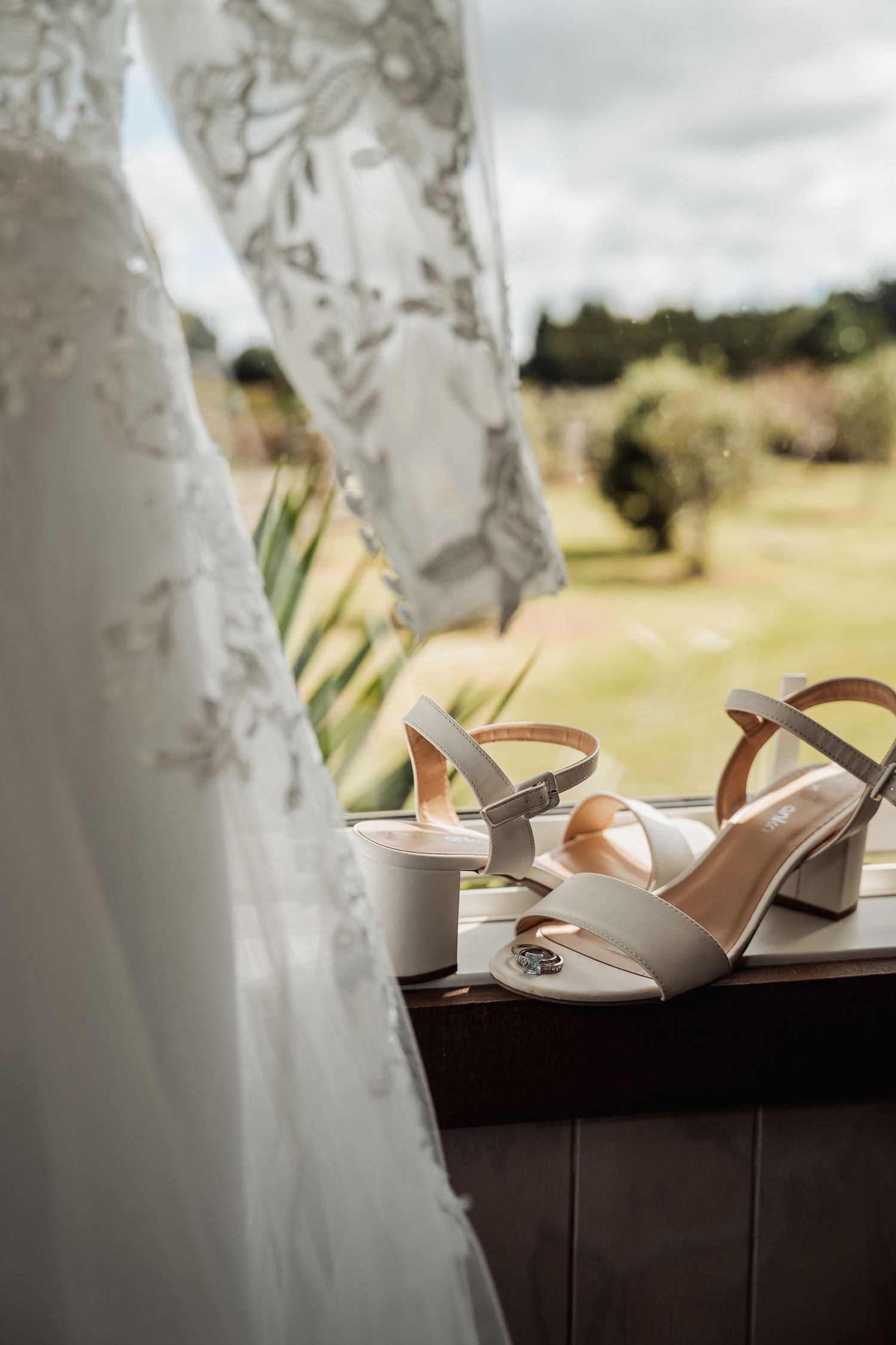 White bridal heels and lace wedding dress details against a soft outdoor background.